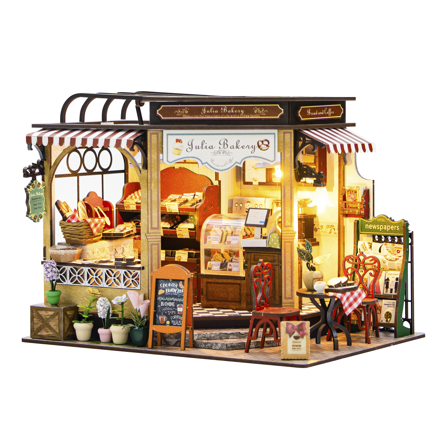 Panetteria in miniatura con pane, pasticcini e caffè. Include tavoli, sedie, fiori e insegne. Un diorama affascinante e dettagliato.