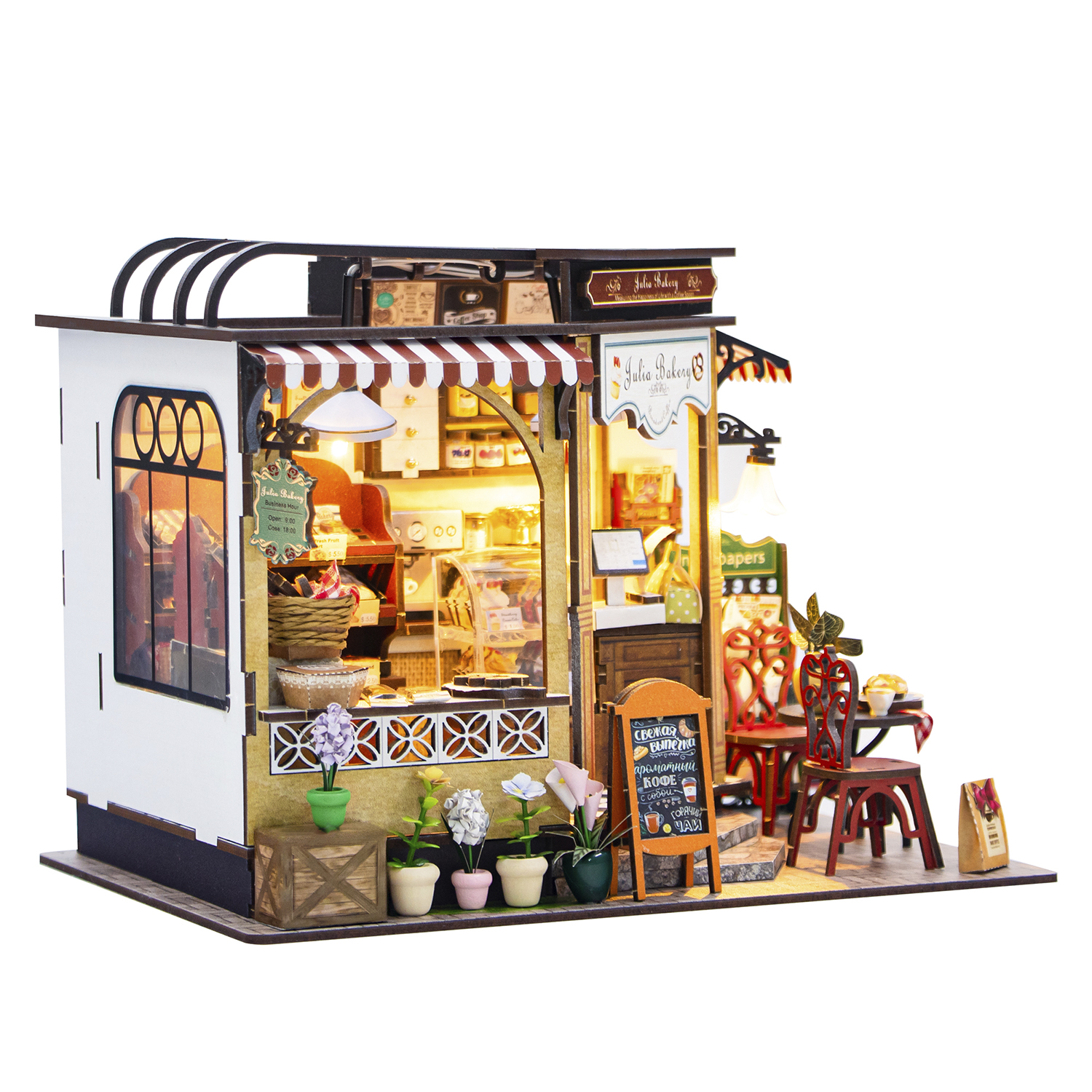 Panetteria in miniatura con tenda da sole rossa e bianca, insegna e tavolino con sedie, fiori e menu.