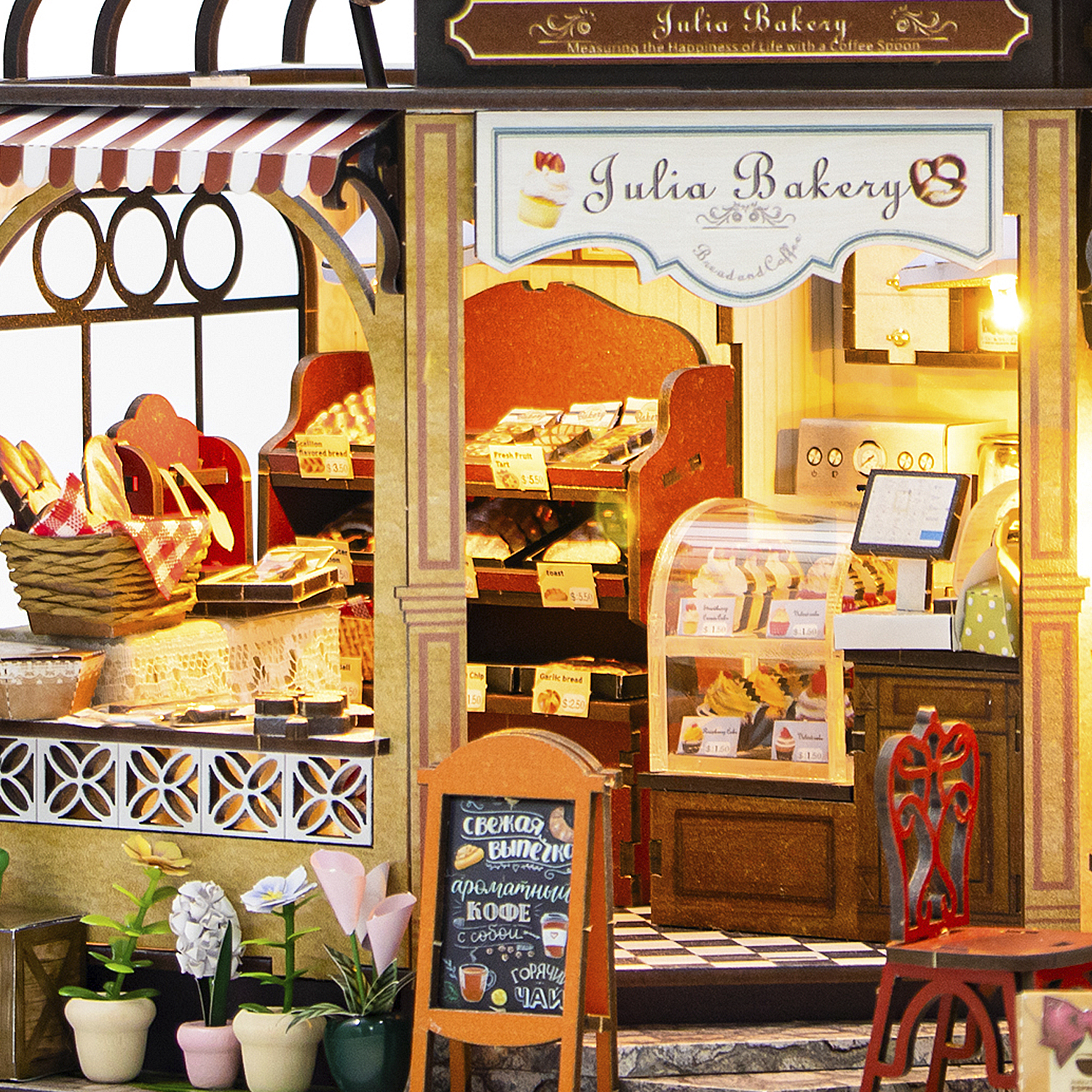 Una panetteria in miniatura con pane, pasticcini e caffè. Un cartello dice 'Julia Bakery'. Ci sono tavoli, sedie, fiori e una lavagna.