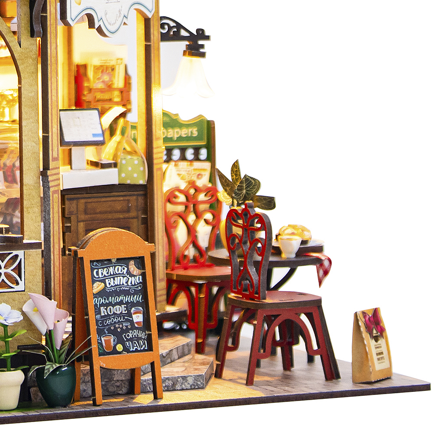Una scena di caffè in miniatura con un cartello, sedie e un tavolo. Ha una luce calda e invitante con cibo e bevande esposte.