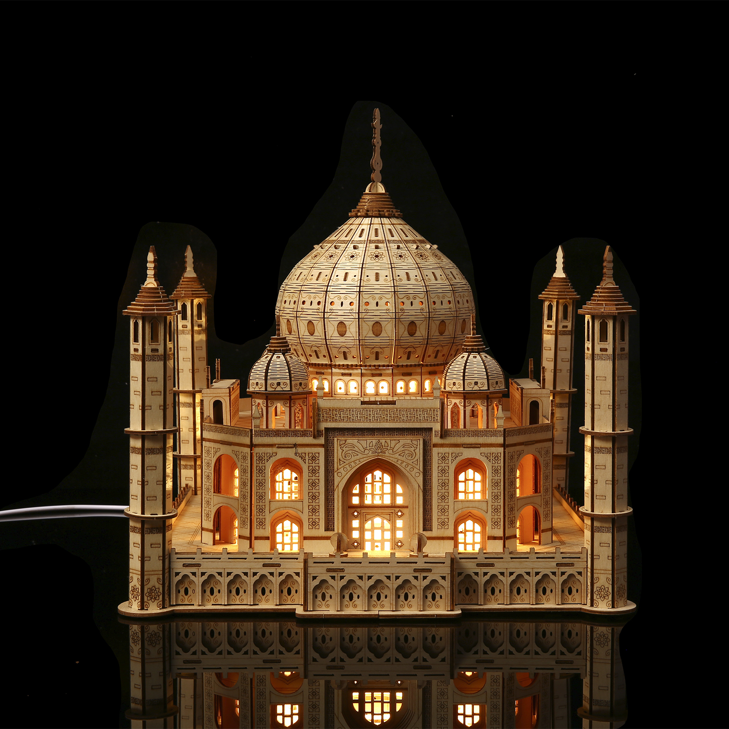 Un modello in legno del Taj Mahal illuminato dall'interno. Si trova su una superficie riflettente su sfondo nero.
