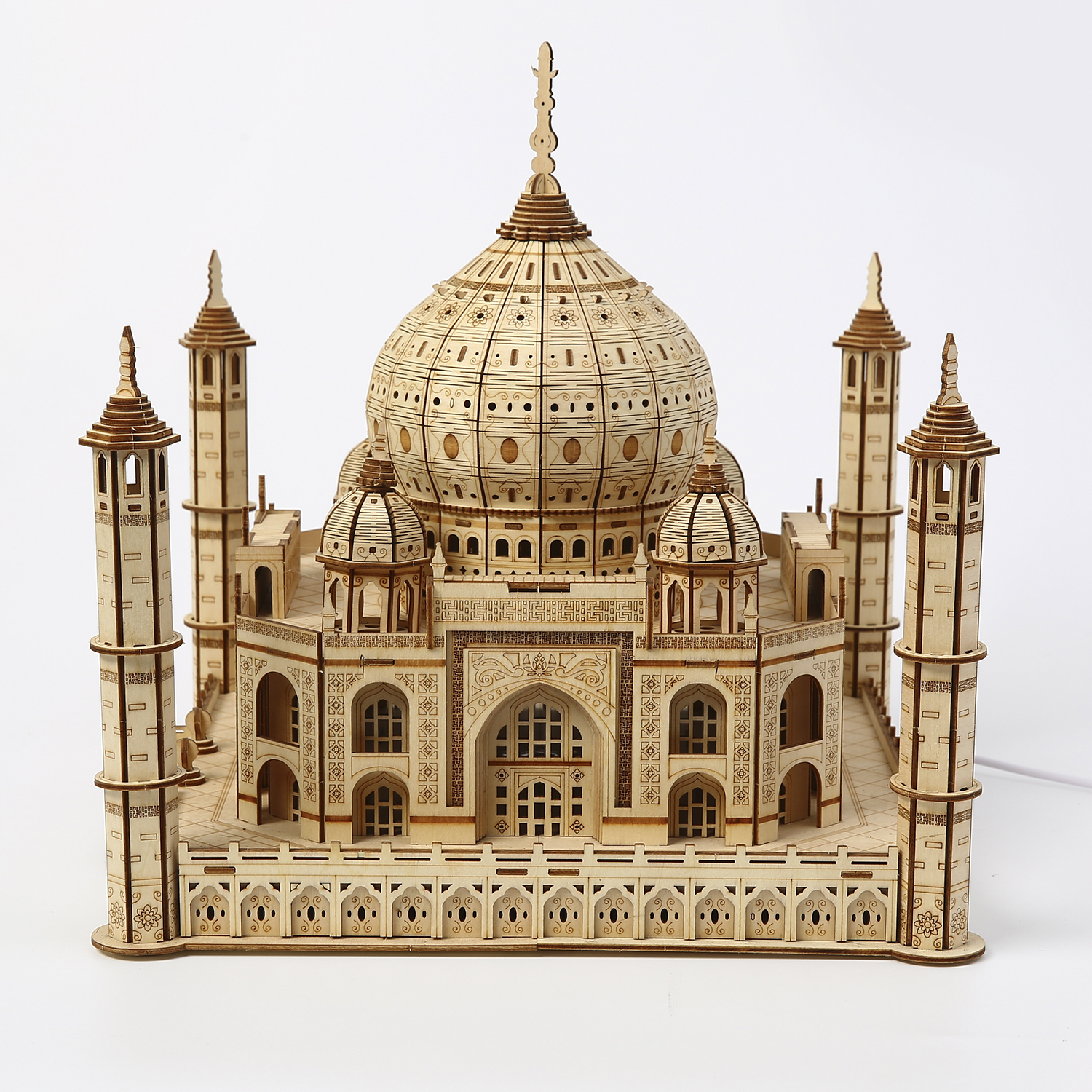Modello in legno del Taj Mahal, dettagli intricati visibili. Il modello ha una cupola centrale, minareti e intagli dettagliati. Su una superficie bianca.