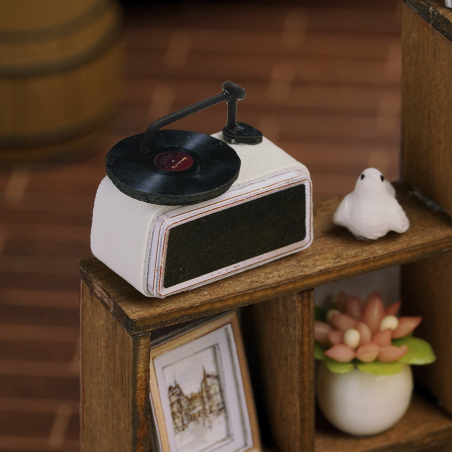Scena in miniatura con un giradischi, una statuetta di uccello bianco e una piccola pianta in vaso su una mensola di legno. È presente anche un'immagine incorniciata.