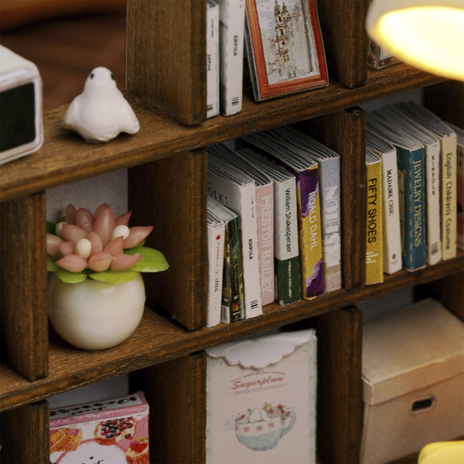 Libreria in legno in miniatura con libri, una statuetta di uccello e un vaso di fiori. I libri hanno titoli diversi. Illuminazione soffusa.