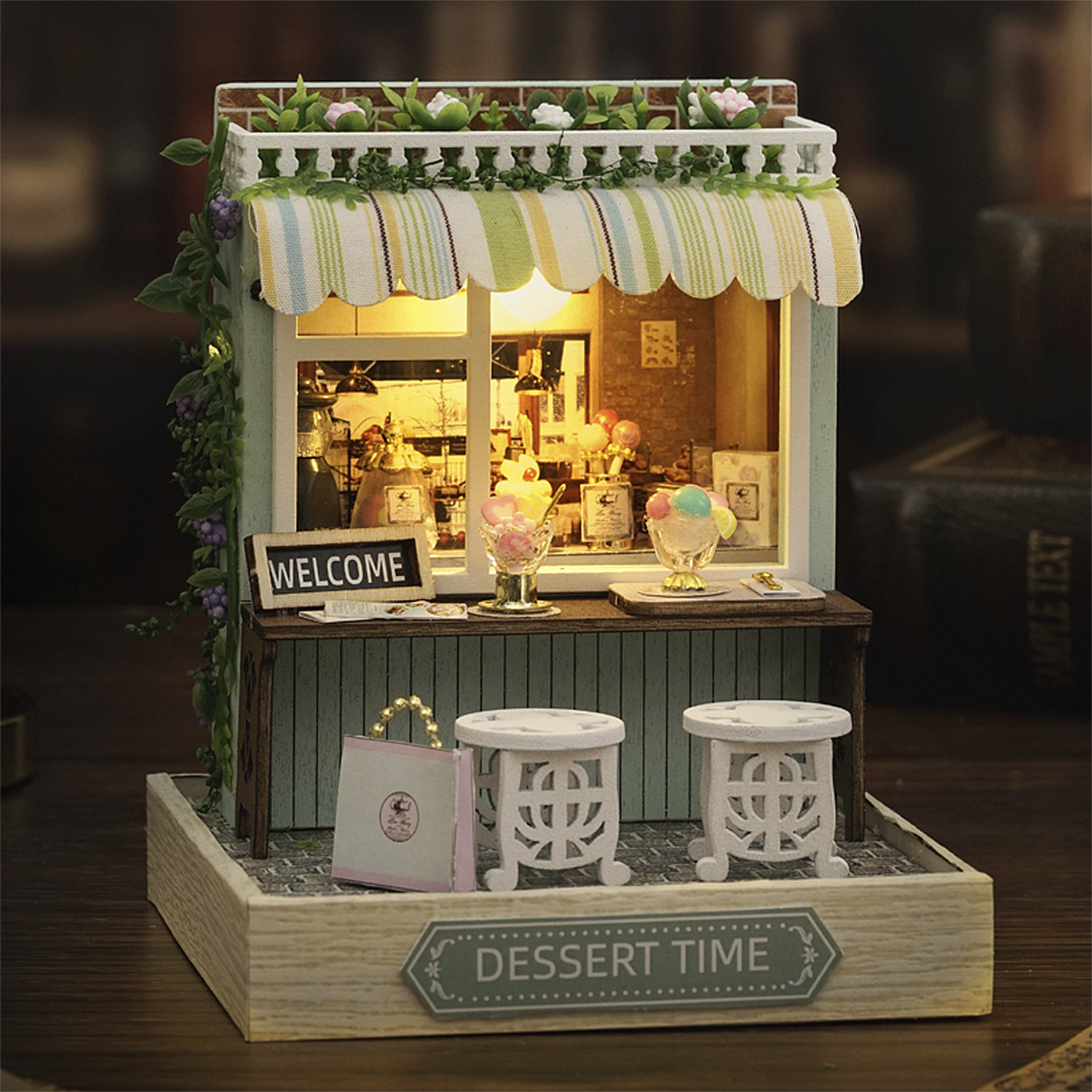 Miniatur-Dessertladen mit Eis und Hockern. Ein Schild sagt 'Willkommen'. Die Markise ist gestreift. Das Schild 'Dessert Time' ist sichtbar.