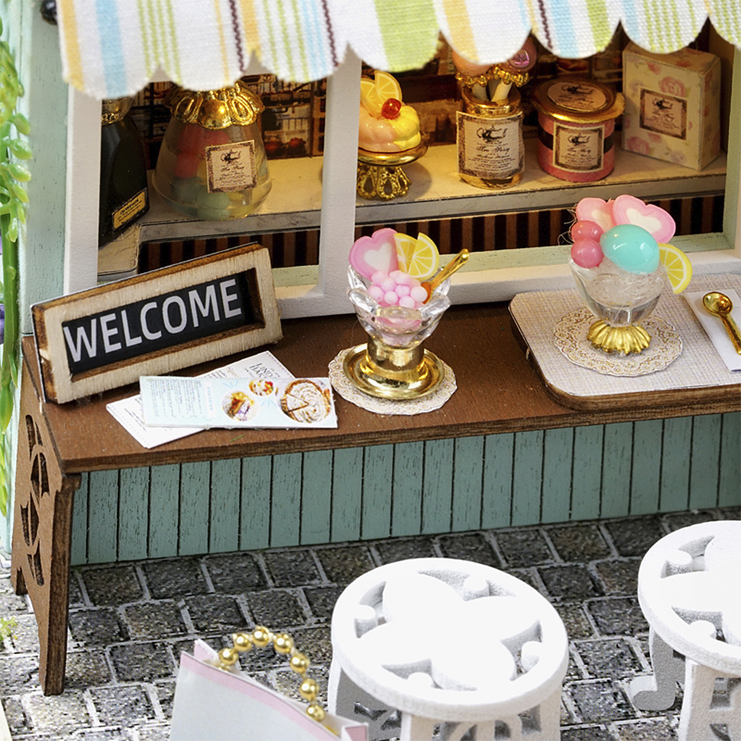 Miniatur-Eisdiele mit Desserts. Ein Willkommensschild und zwei weiße Stühle sind im Vordergrund. Hintergrund hat Regale mit Leckereien.
