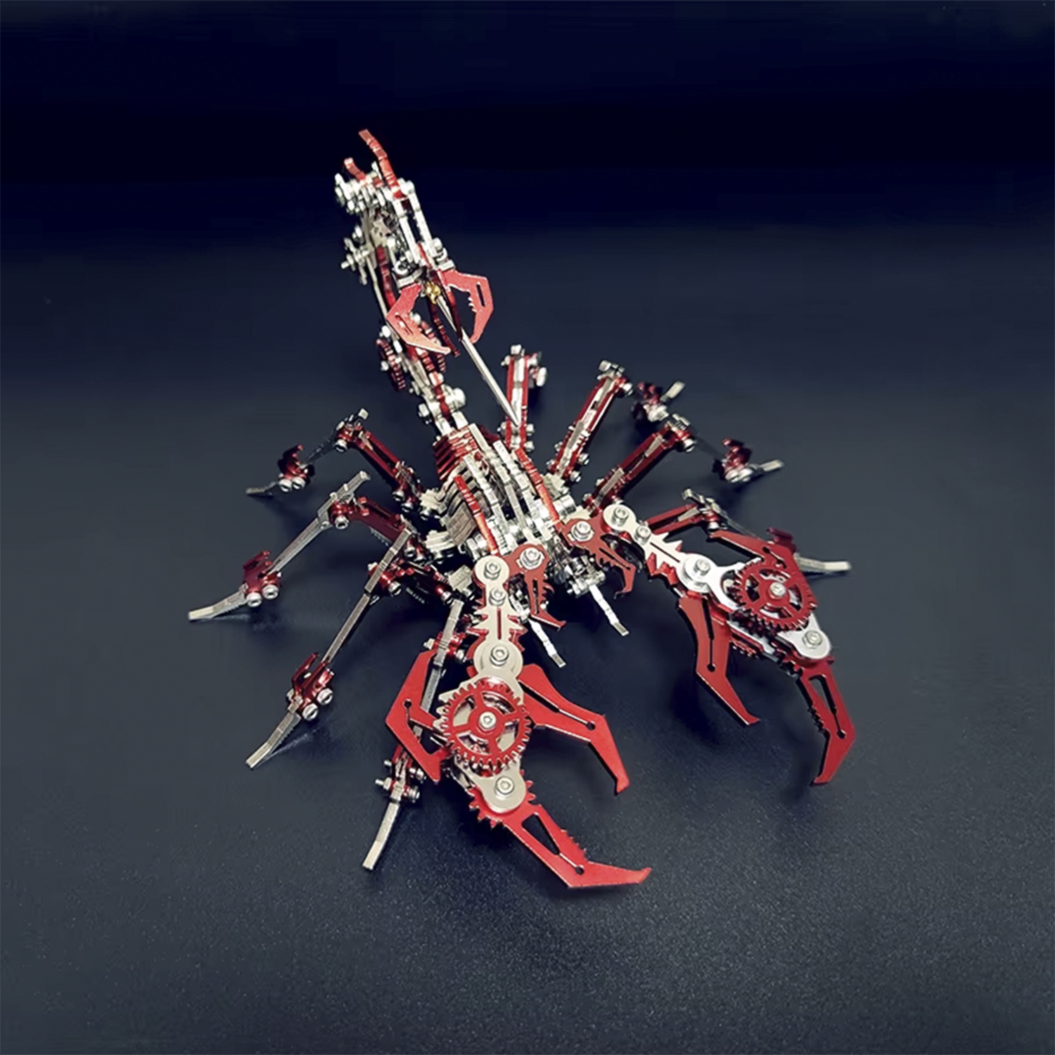 Un modello di scorpione in metallo con parti rosse e argento è su una superficie scura. Il modello ha dettagli intricati, tra cui ingranaggi e artigli.