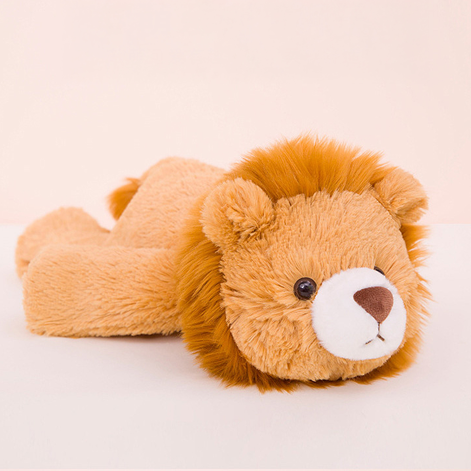 Un leone di peluche è sdraiato su una superficie bianca. Ha pelliccia marrone, muso bianco, naso marrone e occhi scuri. Lo sfondo è rosa.