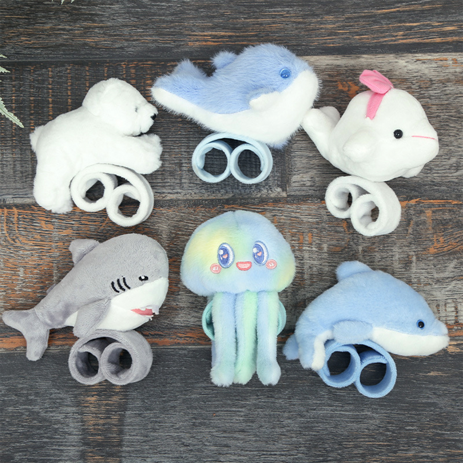L'immagine mostra peluche di creature marine. Un orso polare, uno squalo, una medusa e diverse balene sono su una superficie di legno.