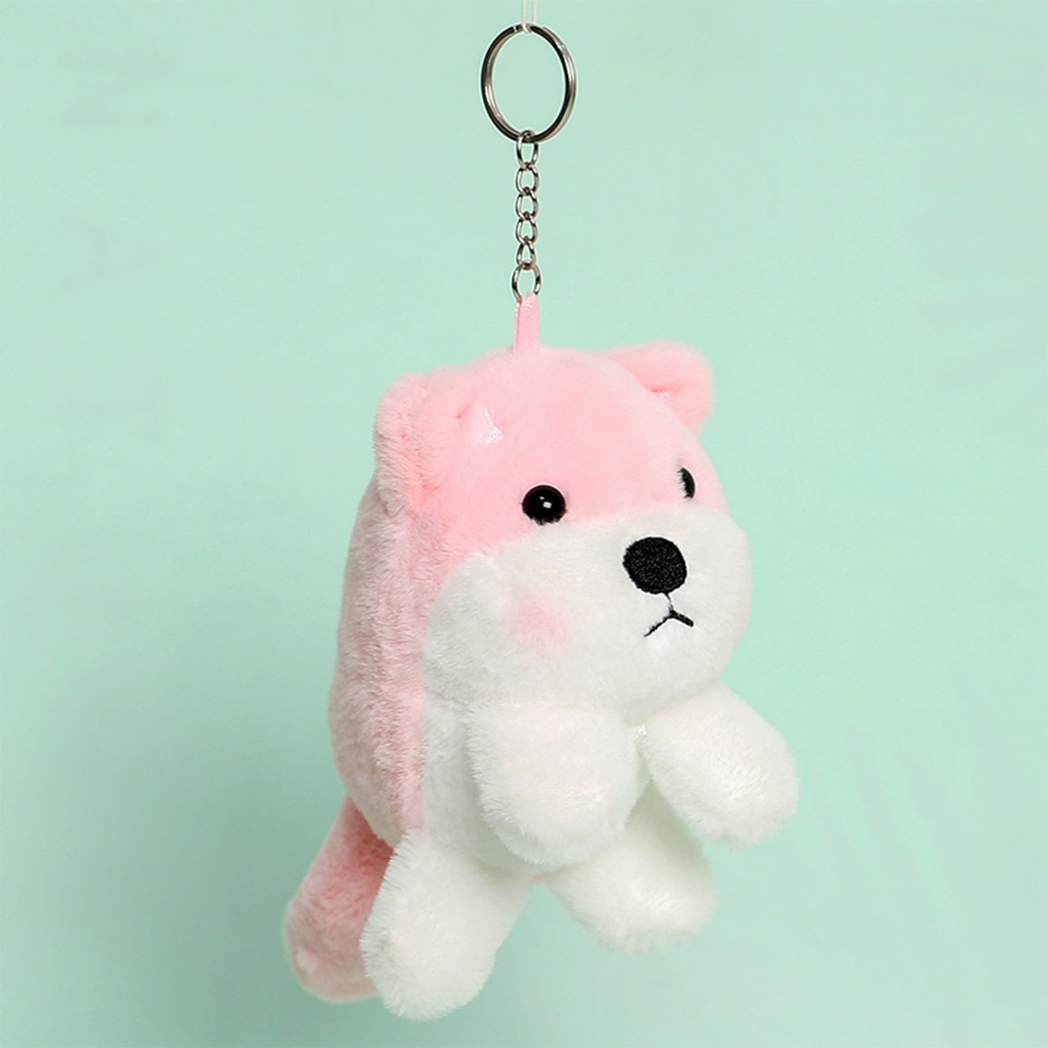 Un peluche rosa e bianco a forma di orso, appeso a un portachiavi su uno sfondo verde acqua.
