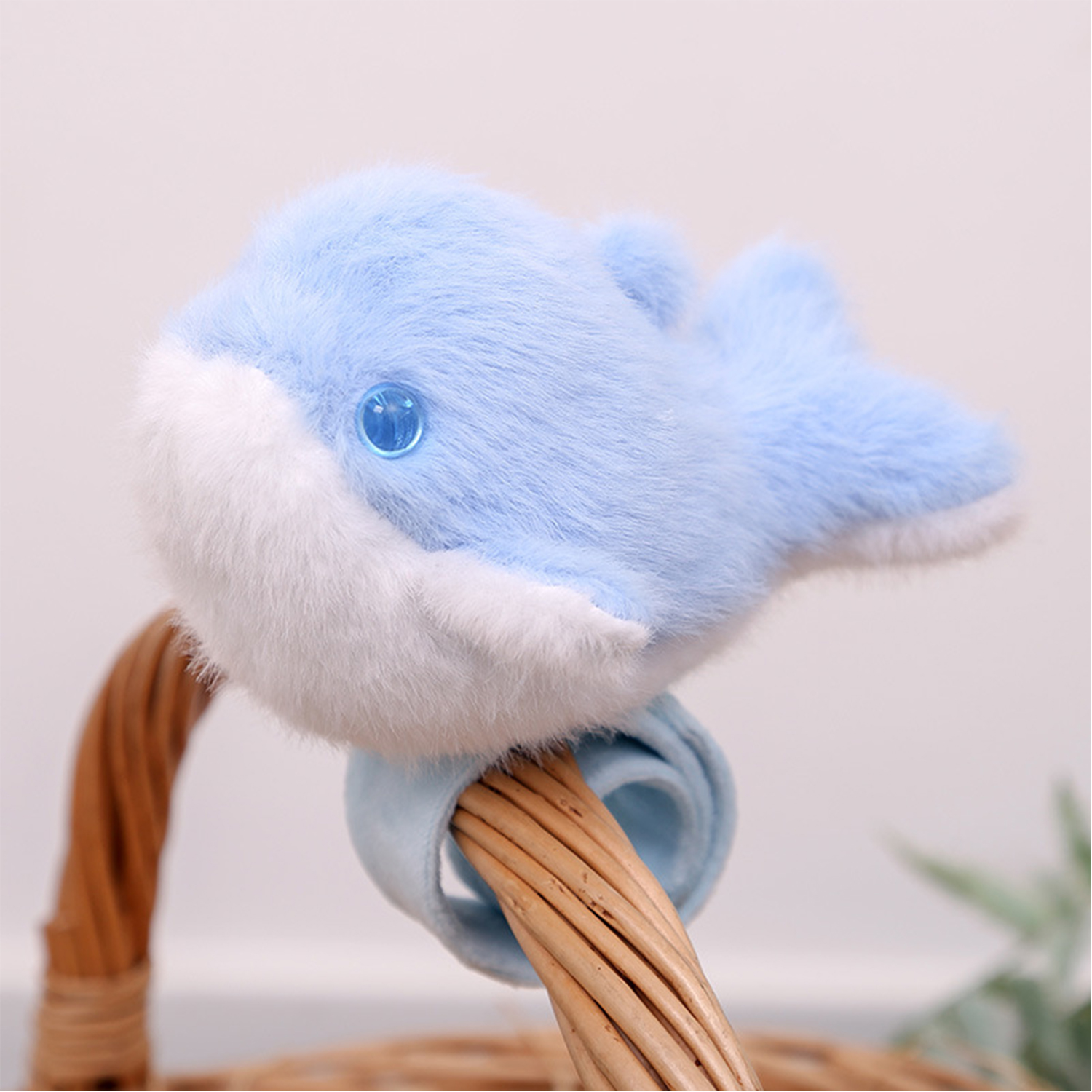 Un giocattolo a forma di delfino blu di peluche con pancia bianca e occhio blu, posto su un cestino di vimini.