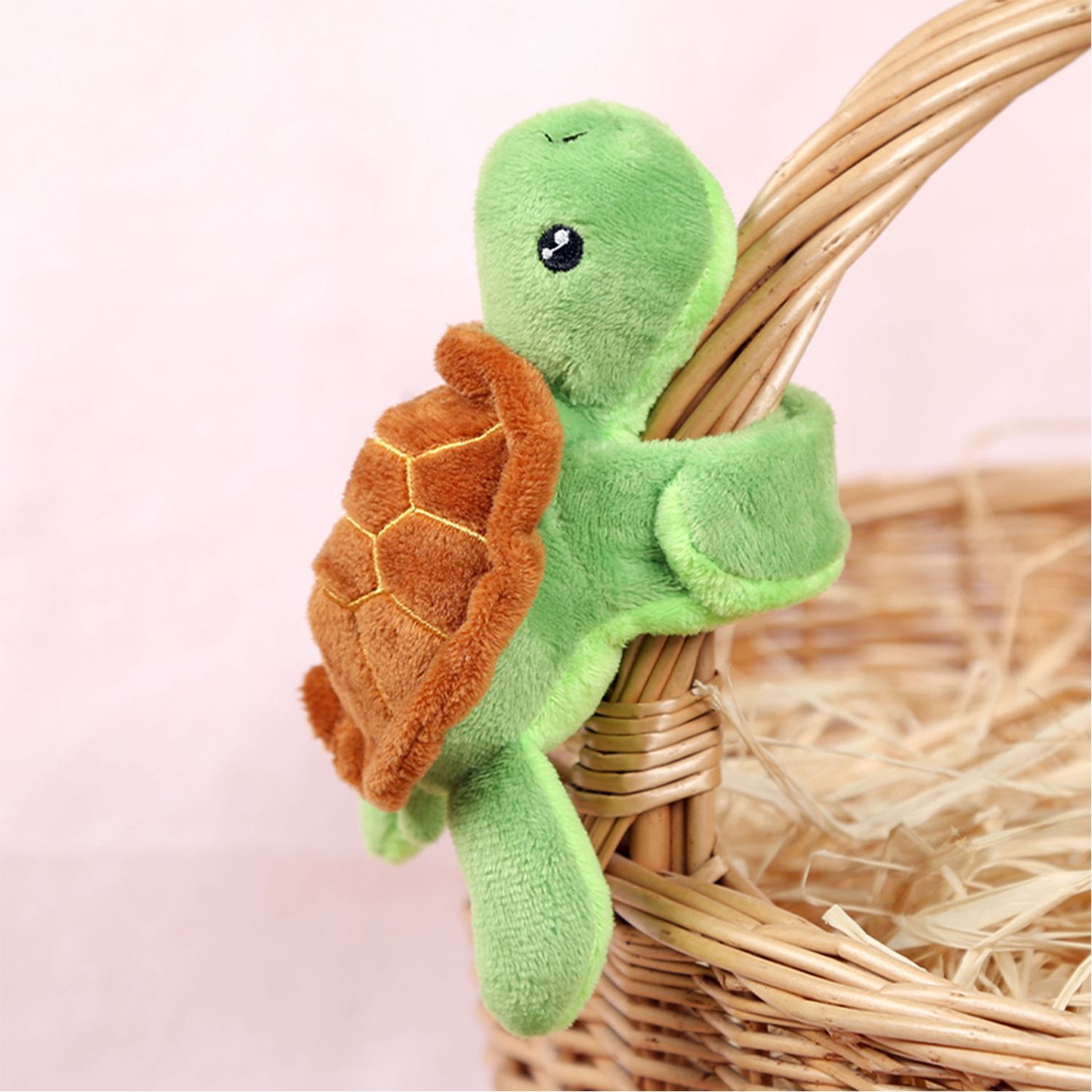 Un peluche di tartaruga verde si aggrappa a un cestino di vimini. La tartaruga ha un guscio marrone ed è circondata da paglia.