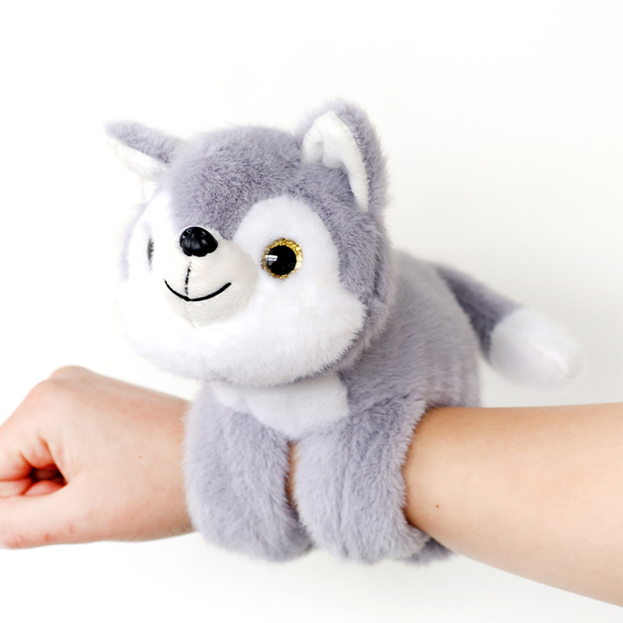 Un giocattolo a forma di lupo di peluche è su un braccio. Il lupo è grigio e bianco, con naso nero e bocca sorridente.