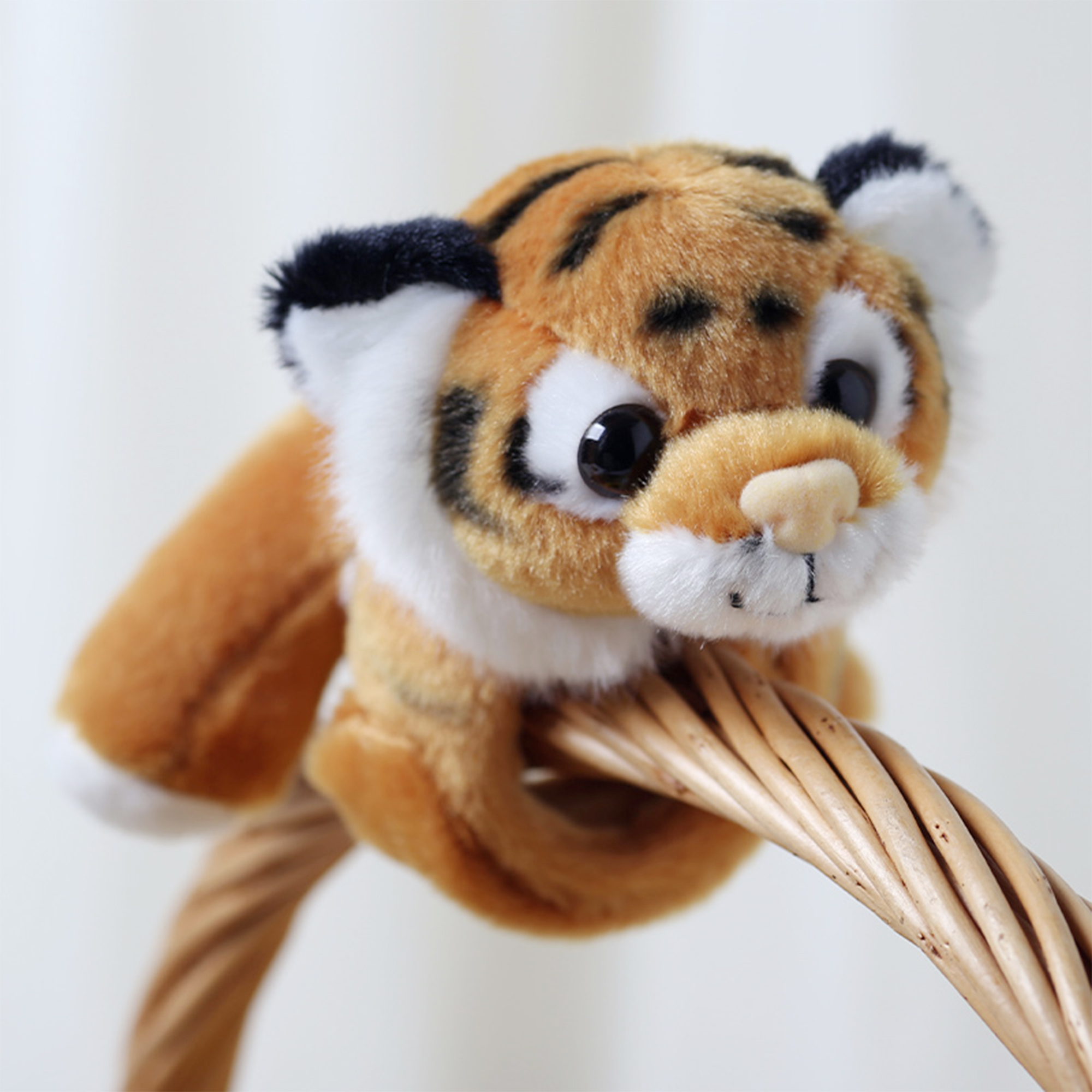 Un cucciolo di tigre di peluche con pelliccia arancione, strisce nere e accenti bianchi, appollaiato su un cestino di vimini.