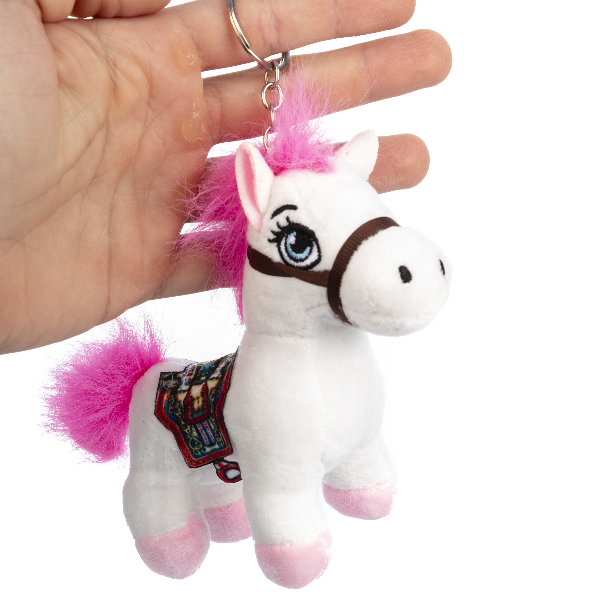 Un peluche unicorno bianco con criniera e coda rosa, tenuto in mano. Ha una sella e si trova su sfondo bianco.