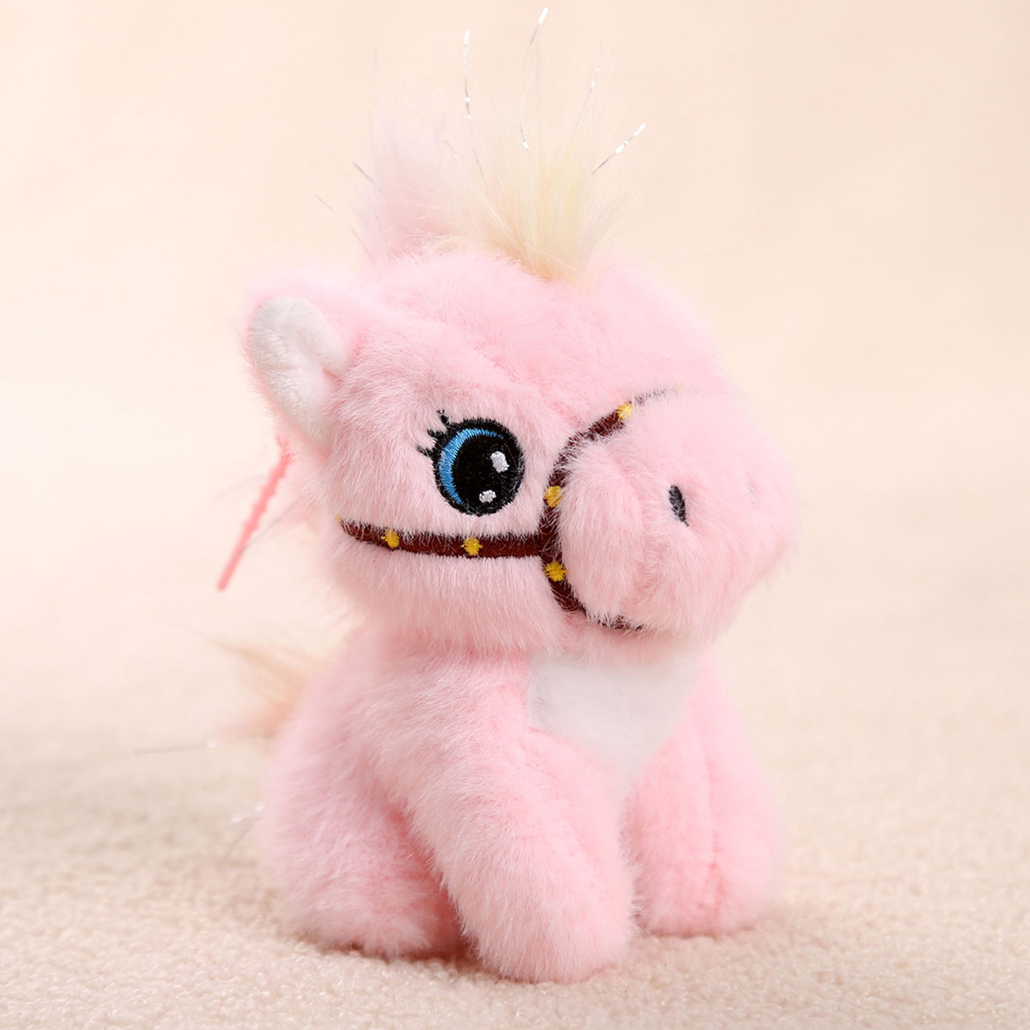 Un cavallo di peluche rosa con occhi blu e una briglia marrone è seduto su una superficie strutturata. Lo sfondo è rosa tenue.