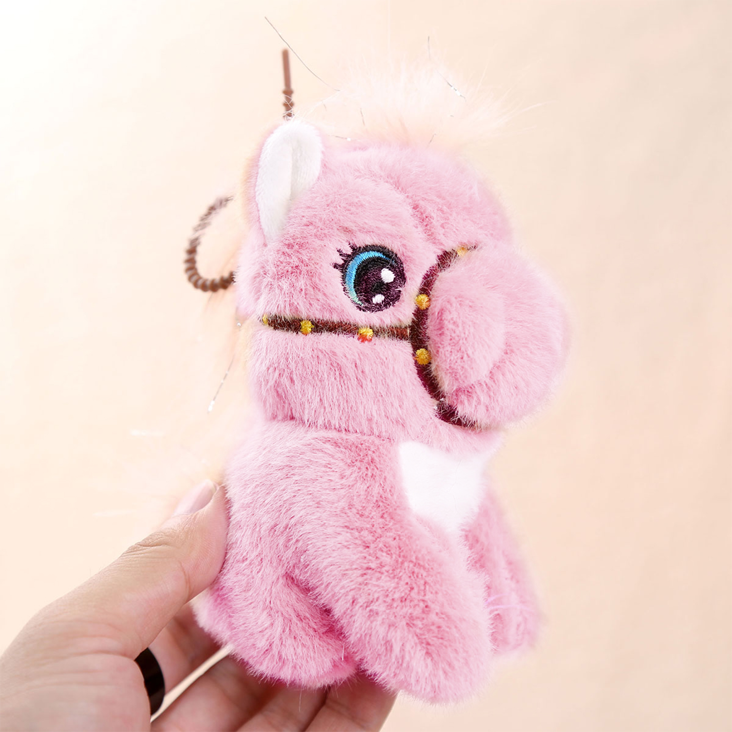 Un giocattolo a forma di cavallo di peluche rosa con un occhio blu e nero, tenuto da una mano. Lo sfondo è un gradiente di arancione chiaro e rosa.