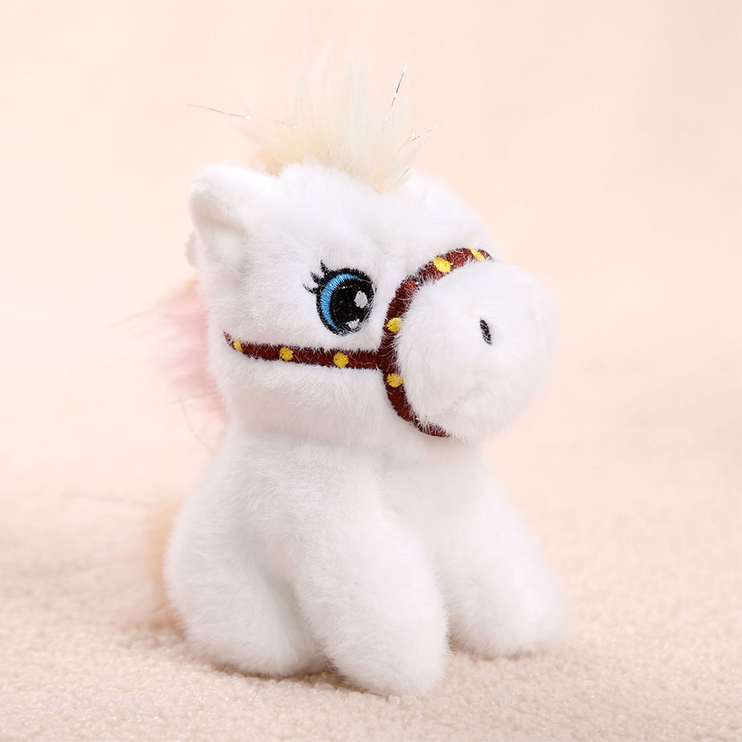 Un cavallo di peluche bianco con criniera e coda rosa. Ha un'imbracatura marrone con punti gialli e grandi occhi blu.