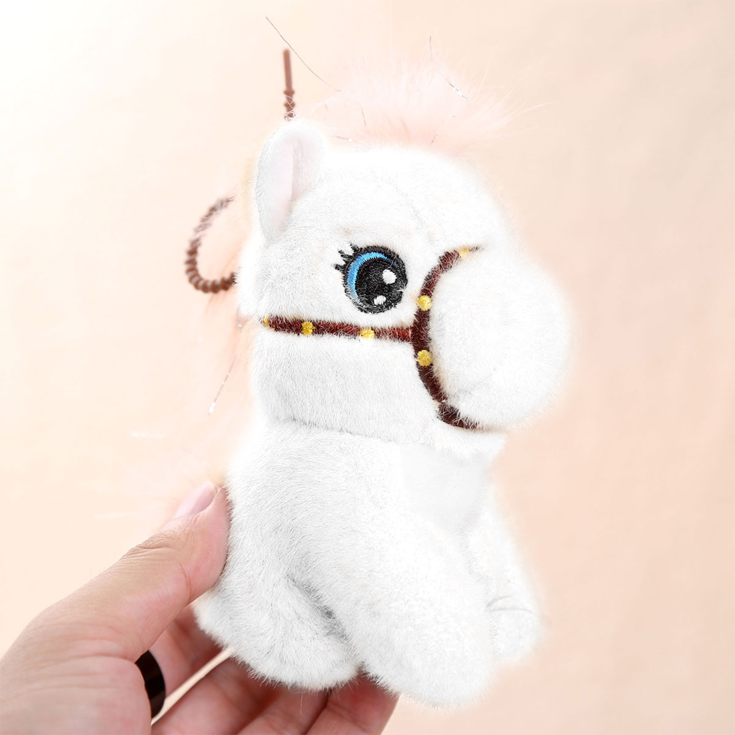 Un giocattolo di peluche a forma di cavallo bianco è tenuto da una mano. Ha occhi blu, un'imbracatura marrone e uno sfondo rosa.