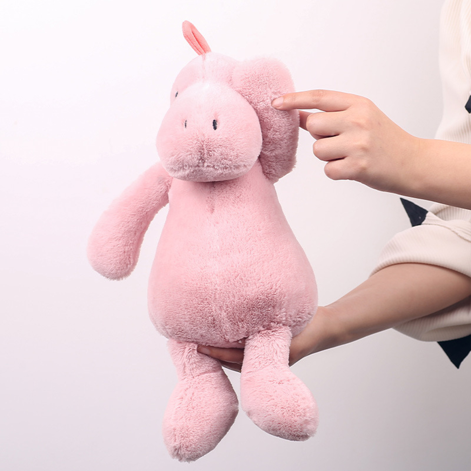 Un peluche rosa è tenuto da una persona. La mano della persona indica l'orecchio del giocattolo. Lo sfondo è bianco.