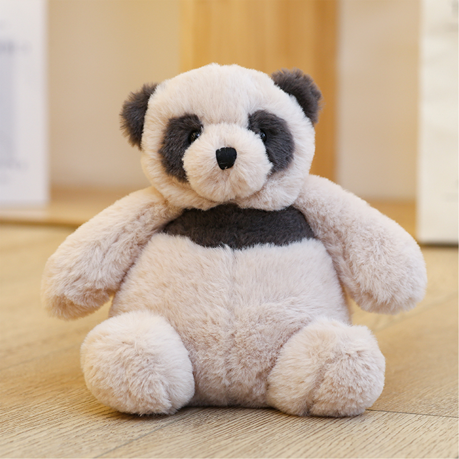 Un peluche a forma di panda con pelliccia rosa, occhi, orecchie e petto neri. È seduto su un pavimento di legno.