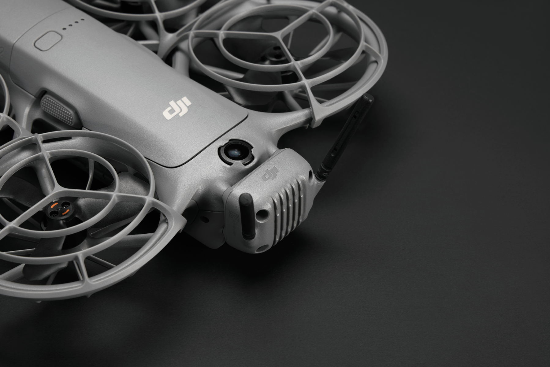 Graue Drohne mit Schutzgittern um die Propeller. Schwarzer Hintergrund. DJI-Logo sichtbar. Antenne ragt heraus.