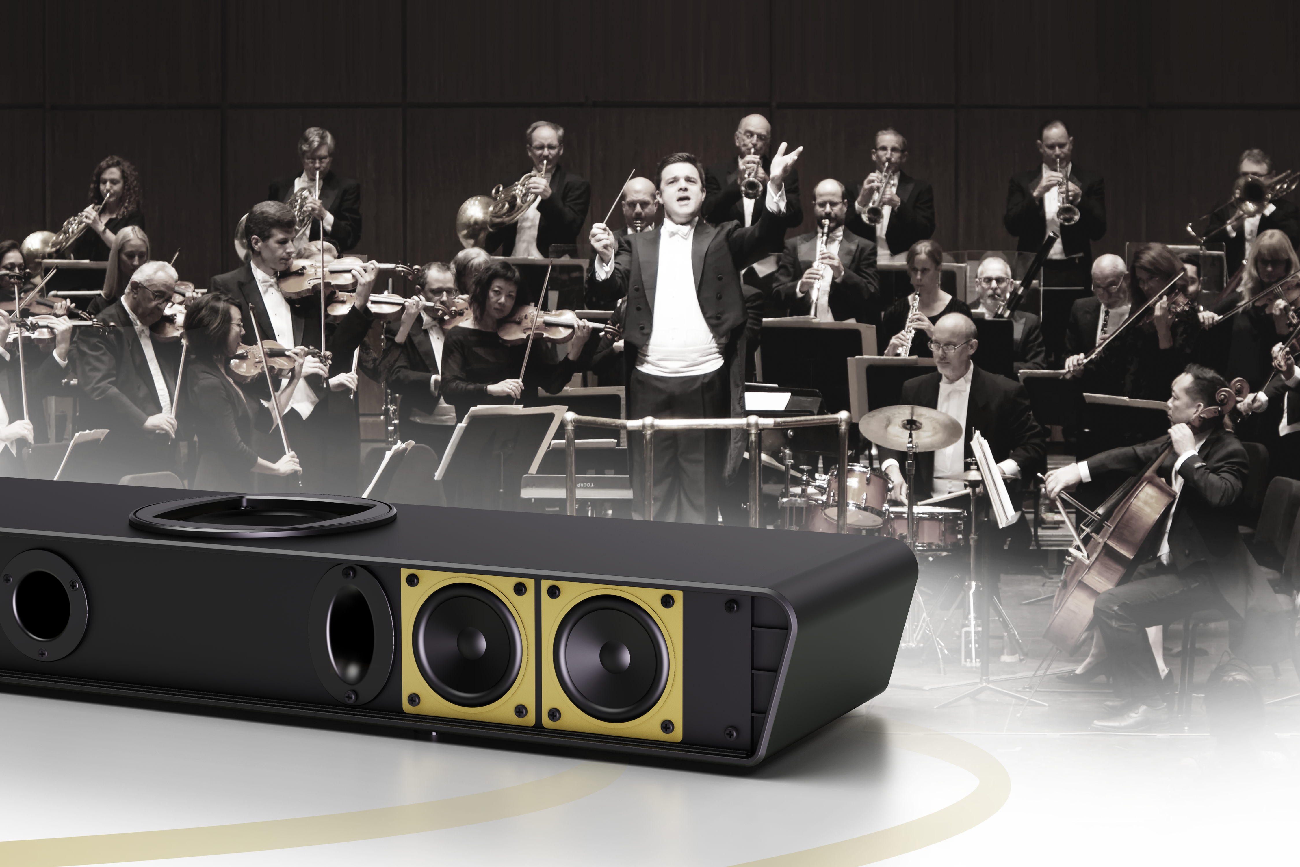 Ein Lautsprecher vor einem Orchester. Der Dirigent leitet die Musiker. Der Lautsprecher ist schwarz und goldfarben.