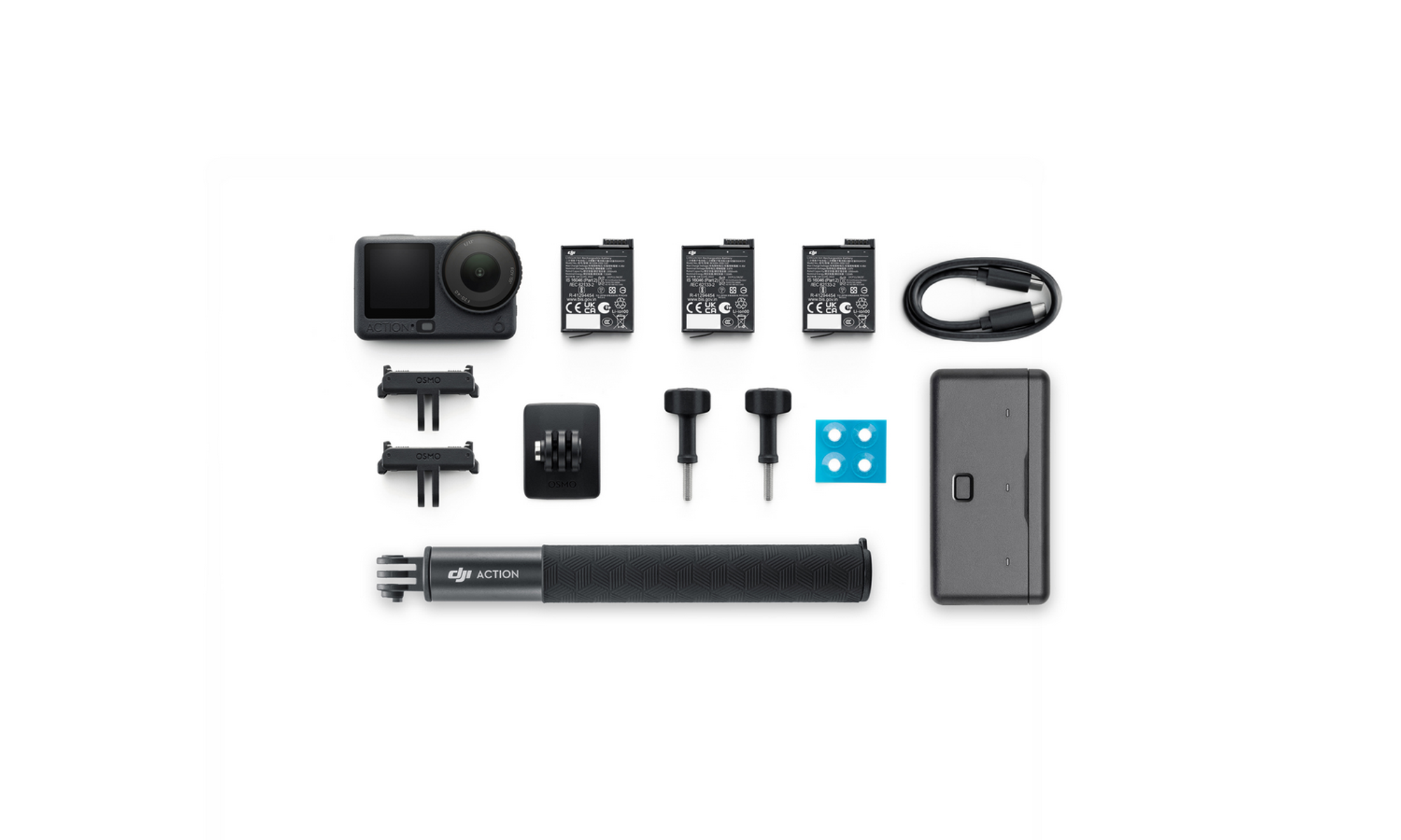 Un kit de cámara DJI Action con cámara, baterías, cargador, mango y accesorios, dispuesto sobre una superficie blanca.