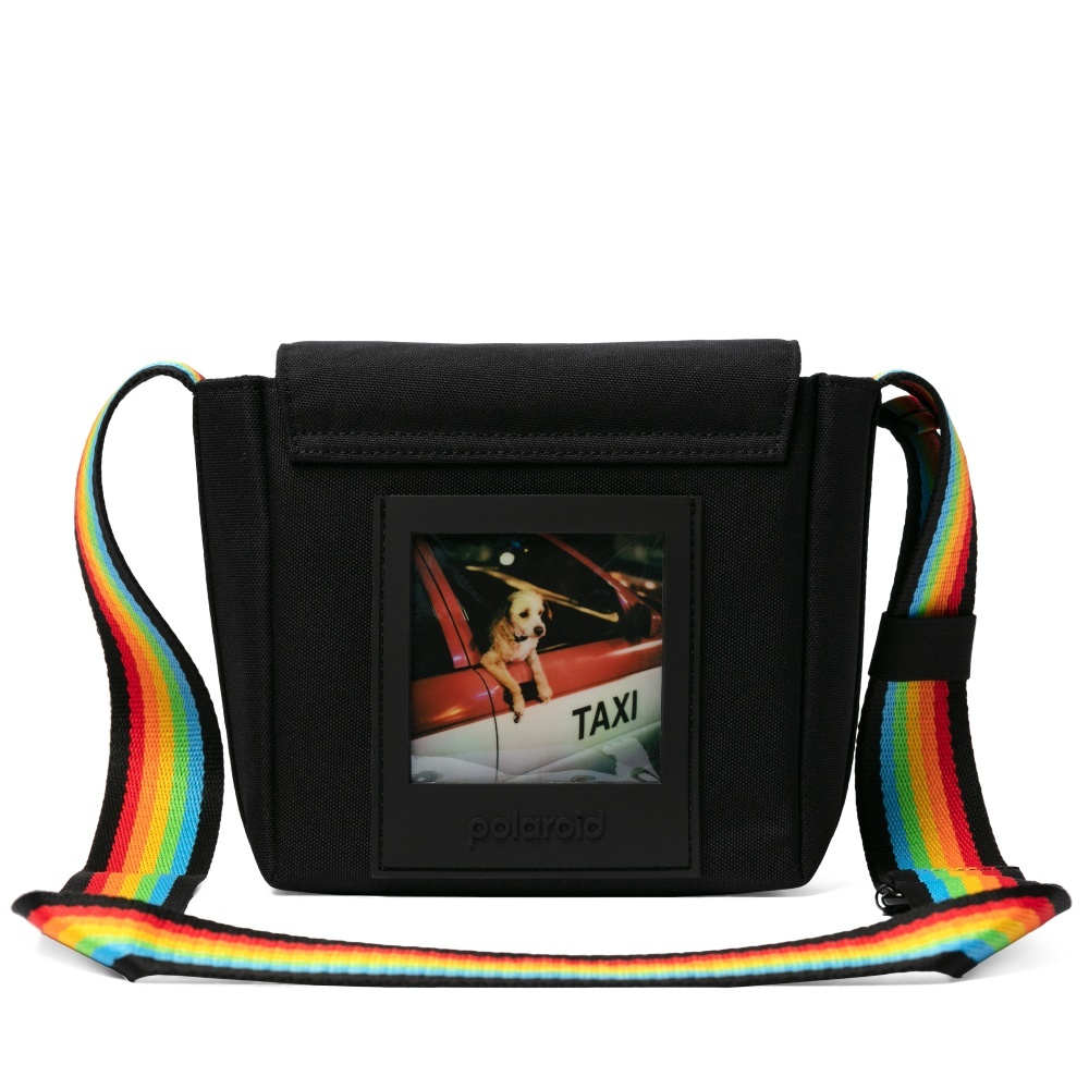 Schwarze Tasche mit Regenbogenriemen und Polaroid-Foto. Das Foto zeigt einen Hund in einem Taxi.