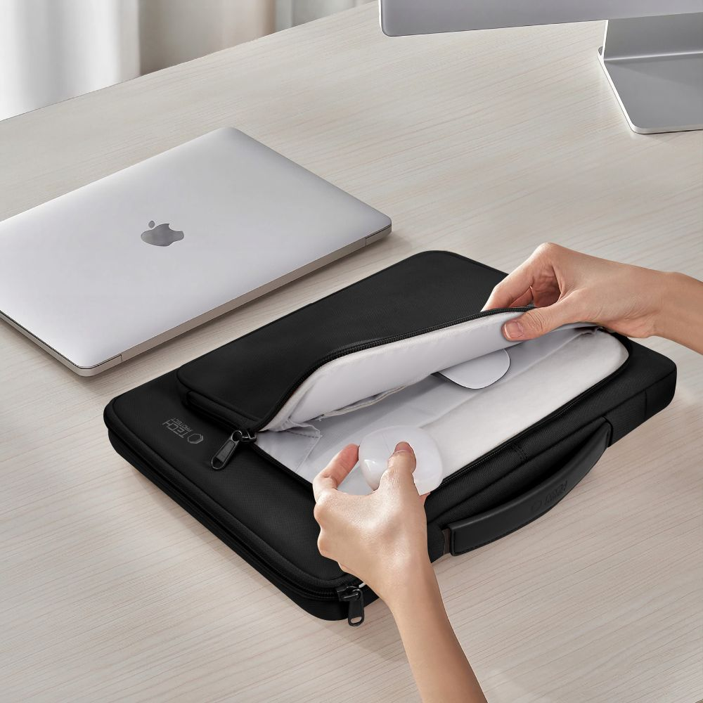 Handen openen een zwarte laptoptas op een houten bureau. Een zilveren laptop is in de buurt. De tas is open en toont een wit interieur.