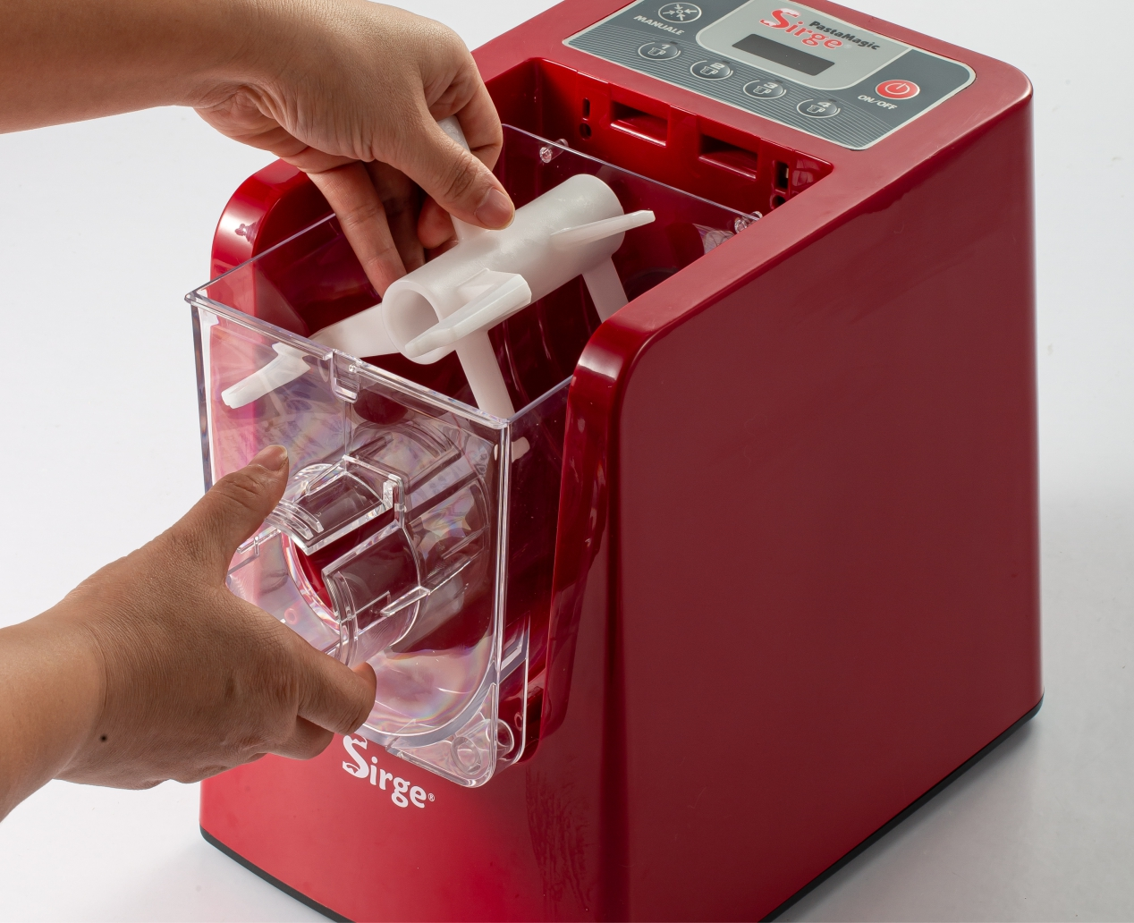 Le mani inseriscono una parte di plastica bianca in una macchina per la pasta rossa. Contenitore di plastica trasparente visibile.