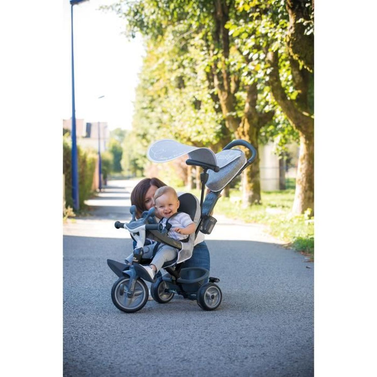 Eine Frau und ein Baby in einem Dreirad. Das Baby lächelt. Bäume säumen den Weg.