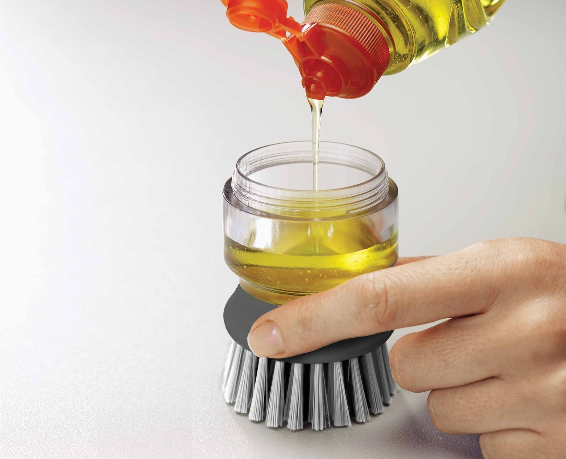 Una mano vierte líquido amarillo de una botella en un recipiente transparente conectado a un cepillo gris.