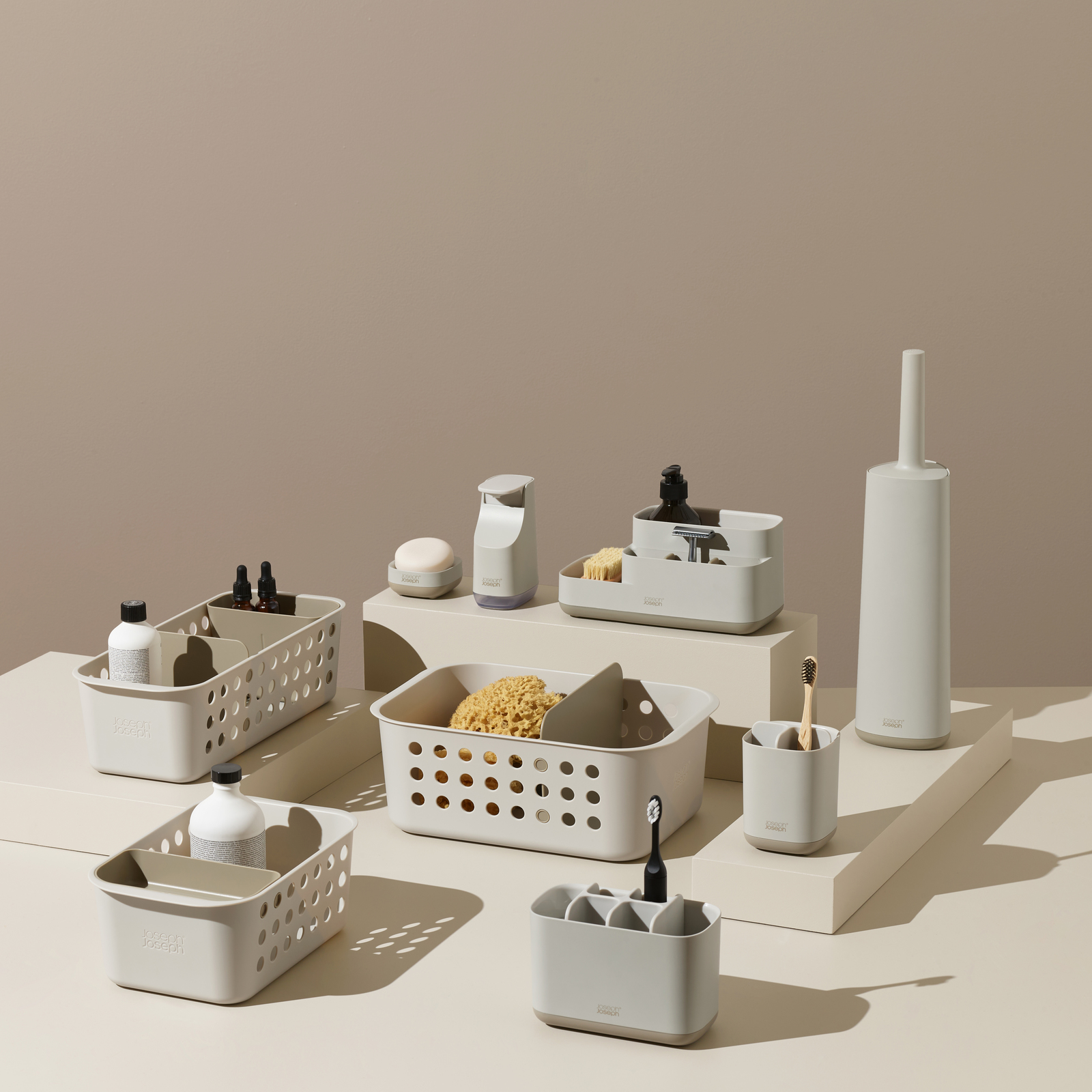 Accesorios de baño grises, incluyendo cestas, dispensadores de jabón, cepillos de dientes y un cepillo de inodoro, dispuestos en plataformas.
