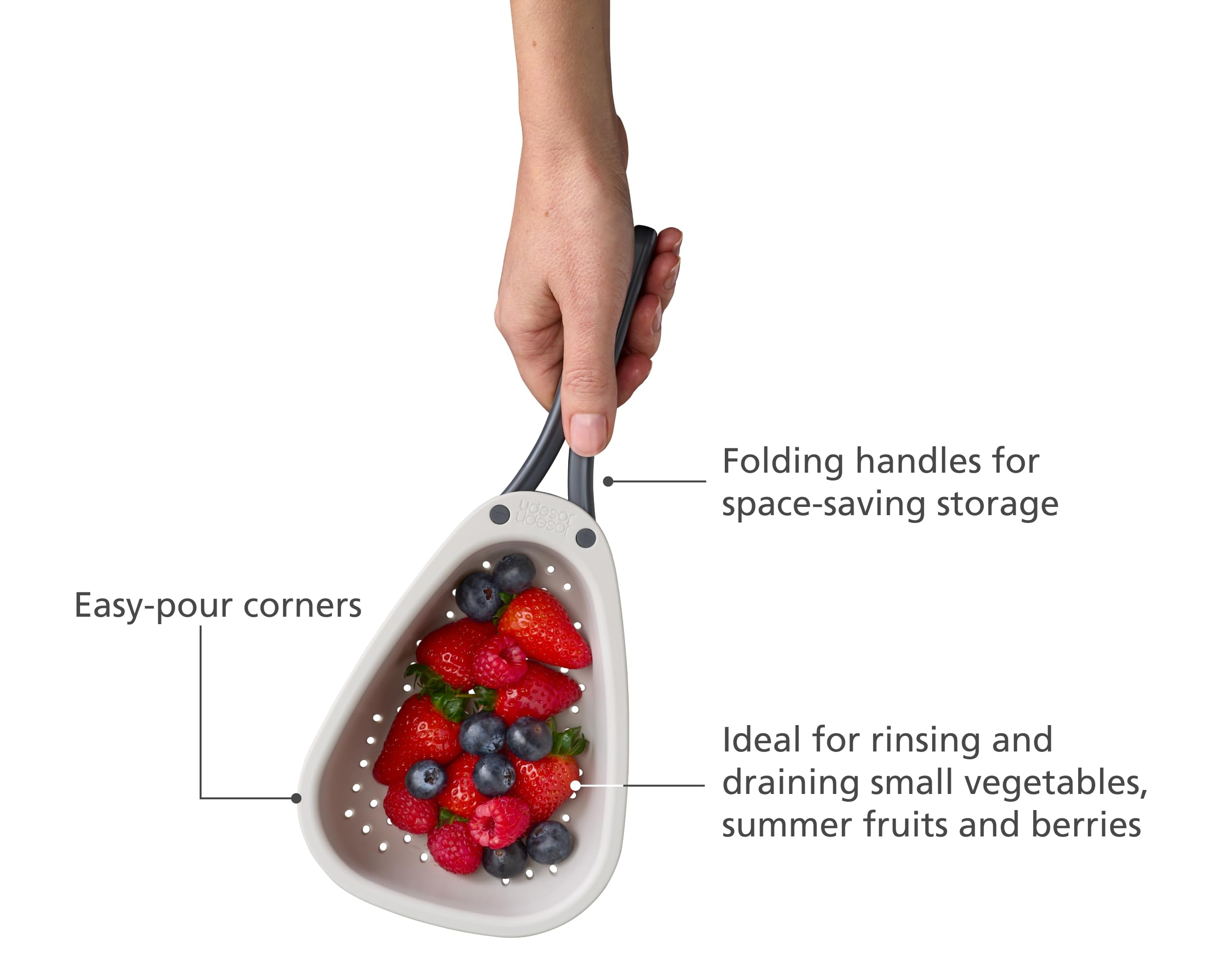 Una mano sostiene un colador blanco lleno de fresas, arándanos y frambuesas. Tiene asas plegables.