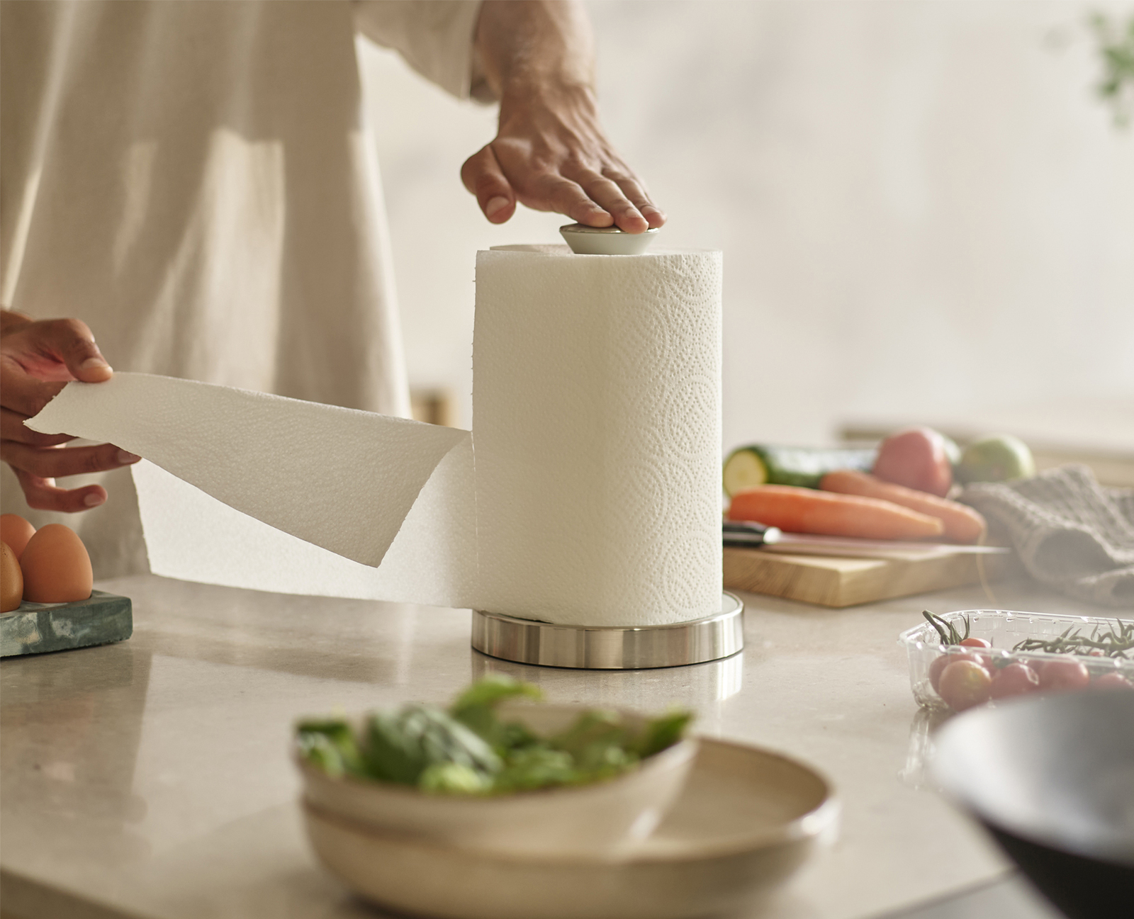 Una persona strappa un tovagliolo di carta da un rotolo. Verdure e uova sul bancone. Ambiente cucina.