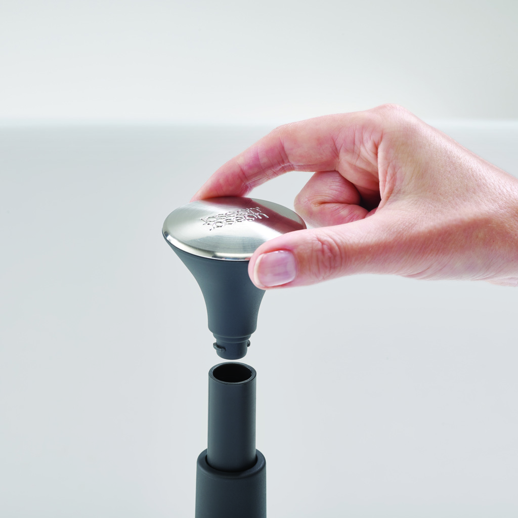 Una mano tiene in mano un utensile da cucina grigio e argento sopra un tubo di collegamento. L'utensile ha una parte superiore metallica ed è parzialmente assemblato.