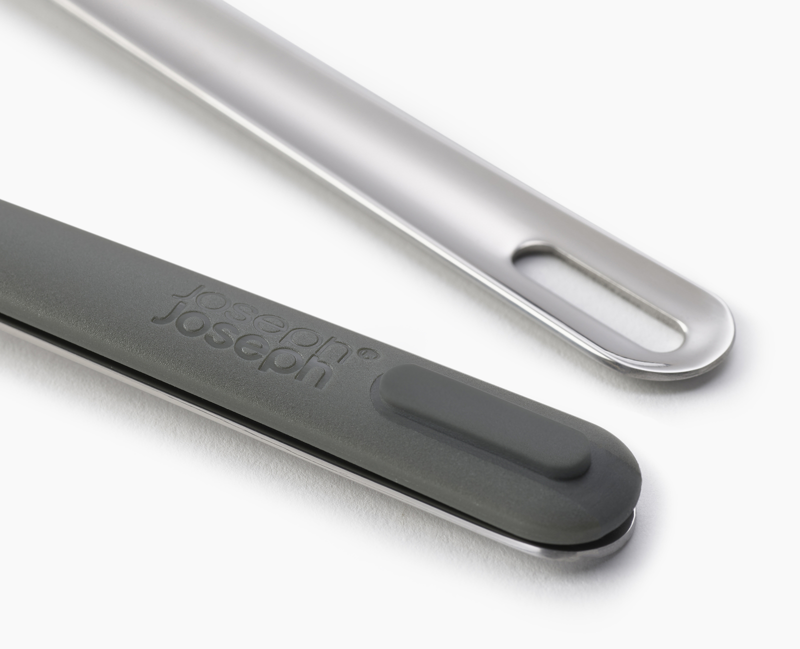Primer plano de utensilios de cocina. Uno es gris con el logo 'Joseph Joseph'. El otro es plateado, con un agujero. Ambos sobre una superficie blanca.