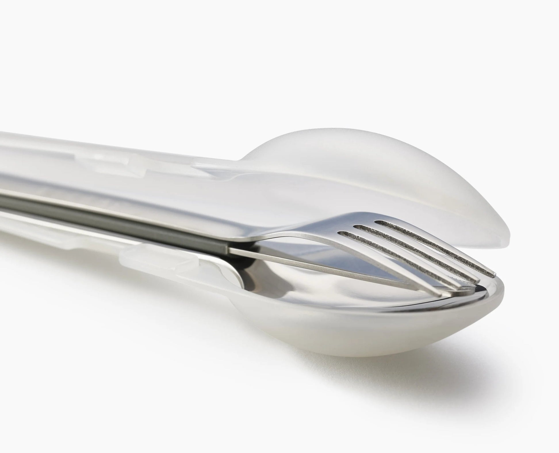 Primer plano de un juego de tenedor y cuchara de acero inoxidable en una funda de plástico transparente, sobre fondo blanco.