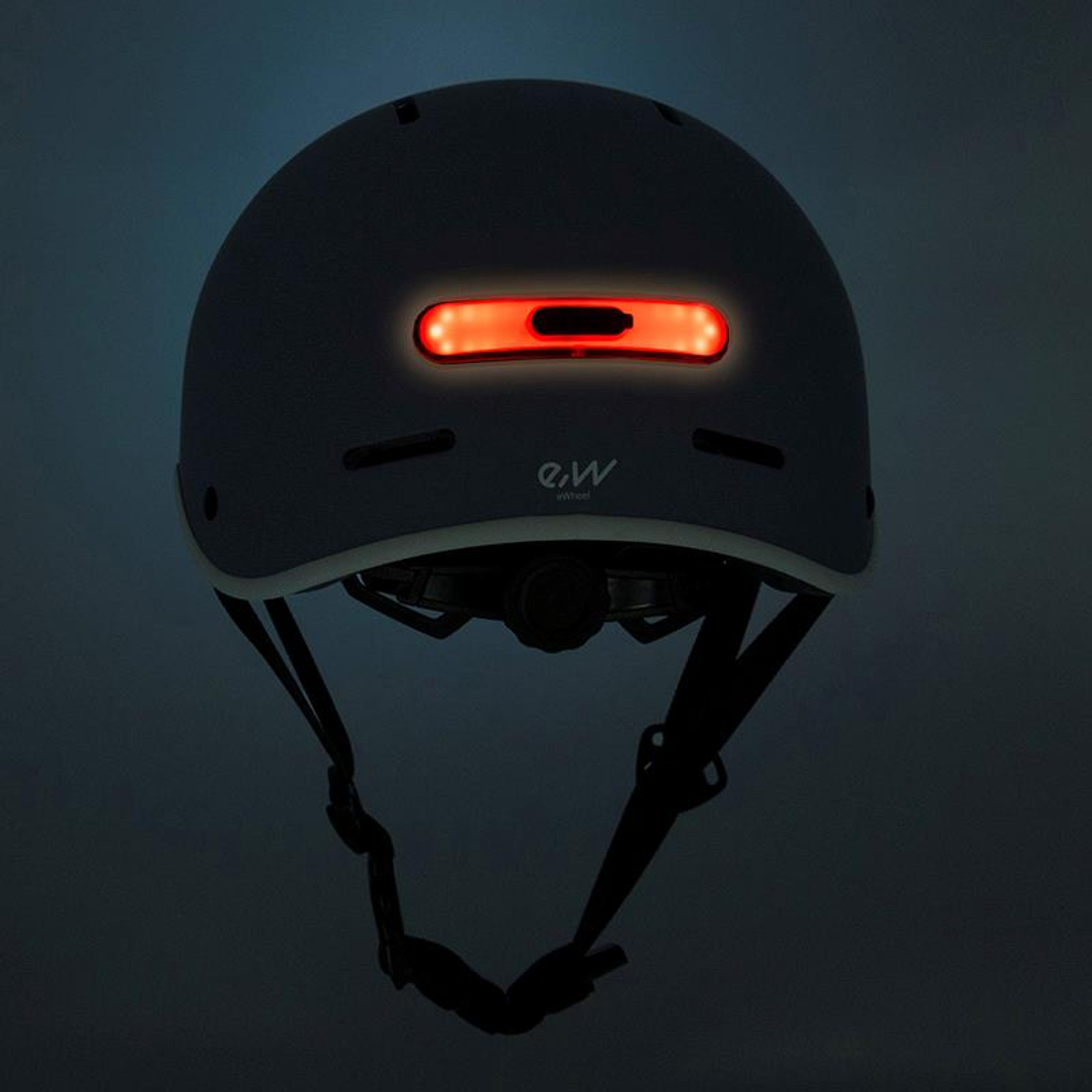 Un casco de bicicleta gris con una luz roja en la parte trasera. Tiene correas negras y un borde blanco.