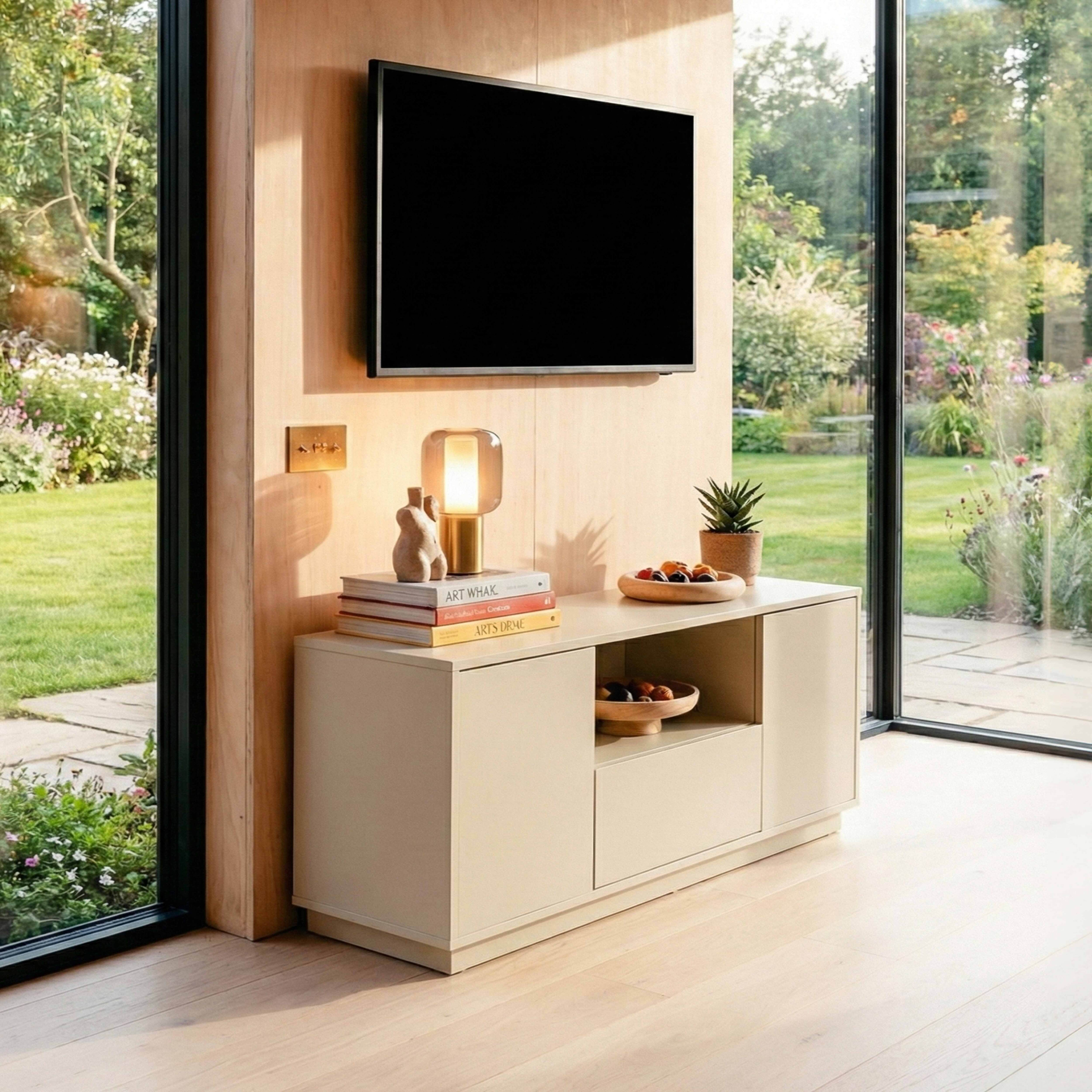 Modernes Wohnzimmer mit Fernseher, Schrank und Blick in den Garten durch ein großes Fenster.