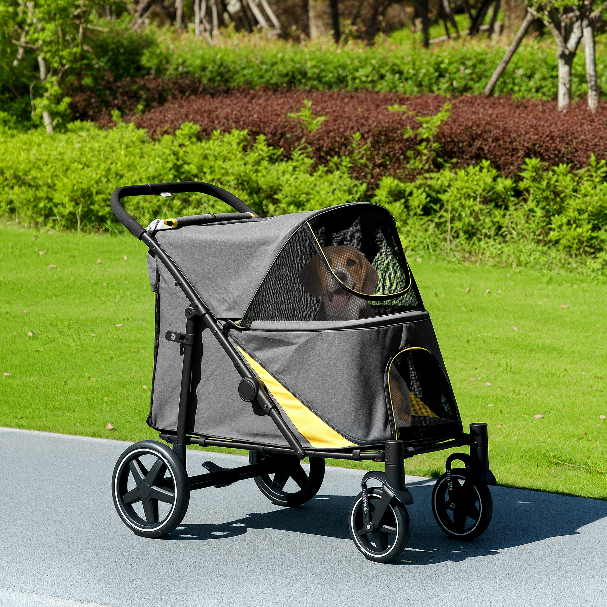 Un cane in un passeggino su un sentiero. Il passeggino è grigio e giallo con ruote nere. Erba verde sullo sfondo.