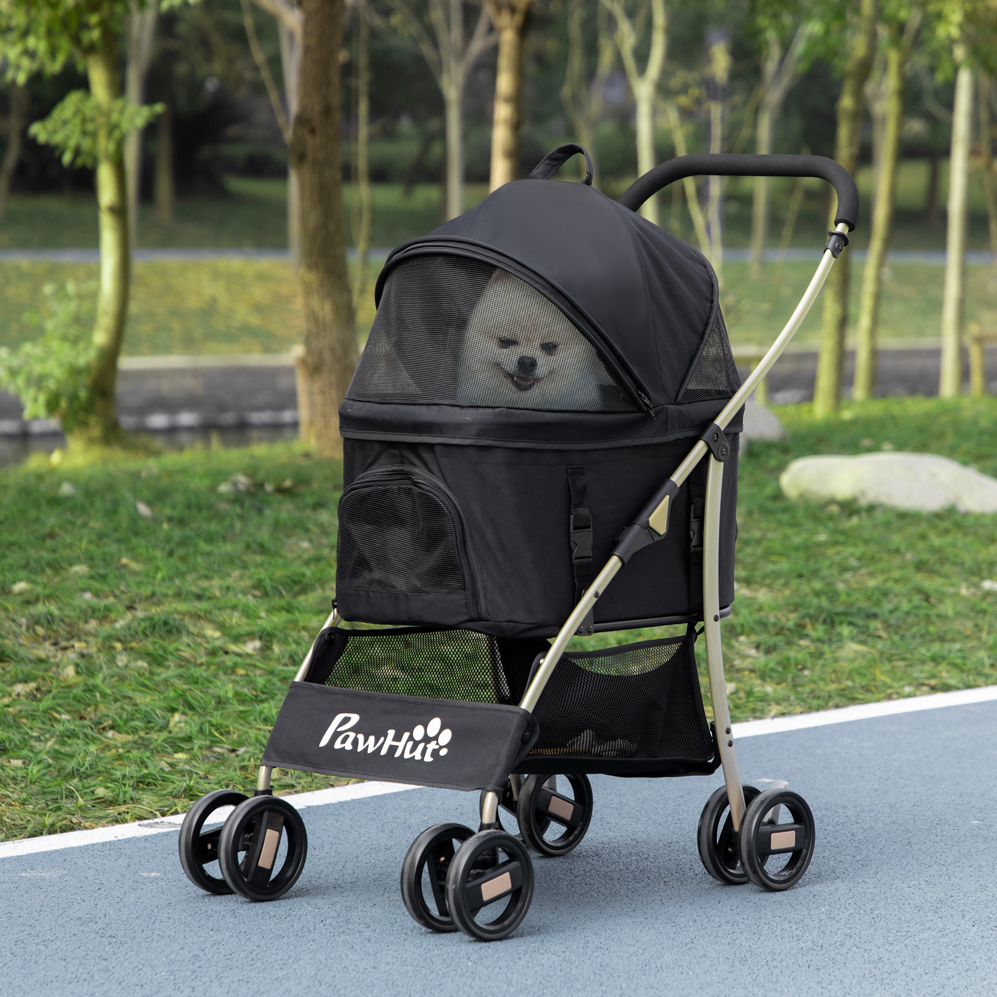 Un cane in un passeggino nero per animali domestici su un sentiero blu. Il passeggino ha una finestra a rete. Gli alberi sono sullo sfondo.