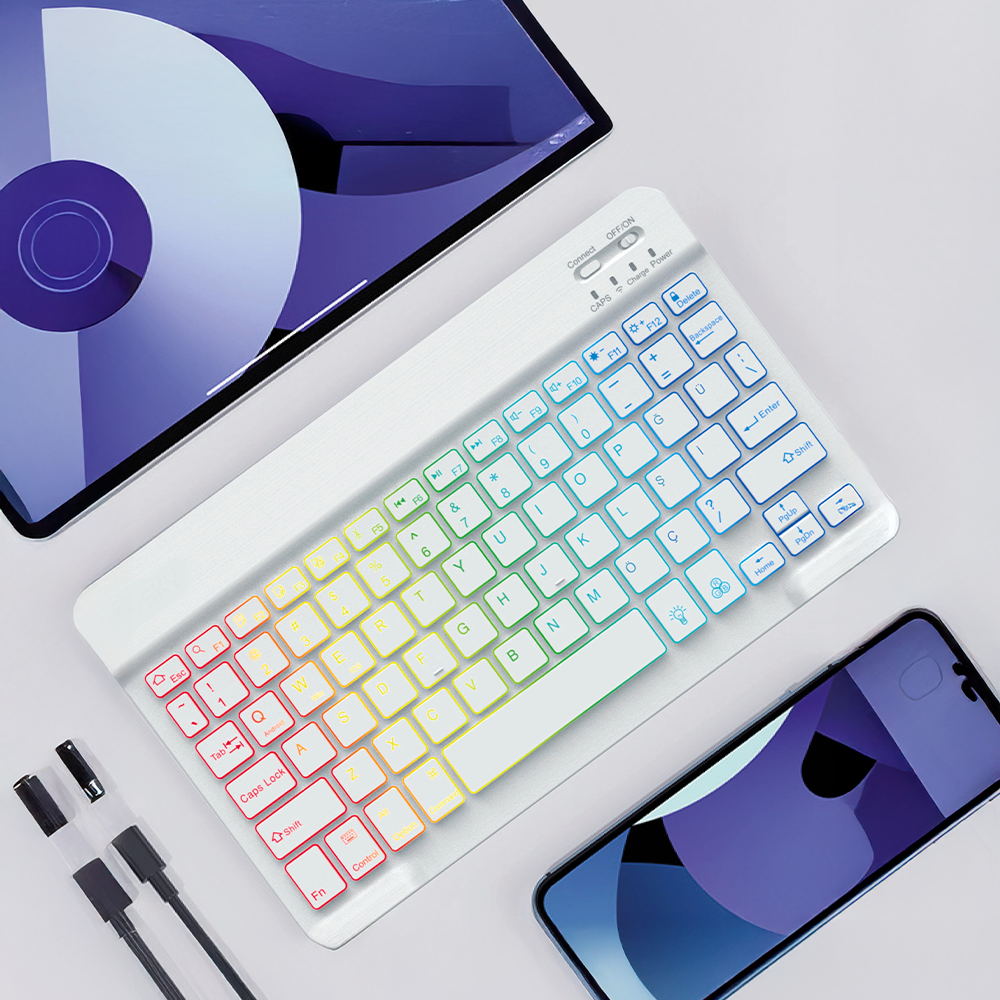 Gökkuşağı renkli tuşlara sahip beyaz bir klavye, bir tablet ve bir telefonun yanında duruyor. Ön planda siyah kablolar var.