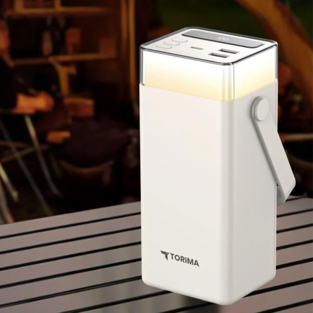 Üstünde ışık olan beyaz bir powerbank. Bir sapı var. Arka planda bir masa ve bulanık bir sahne görülüyor.