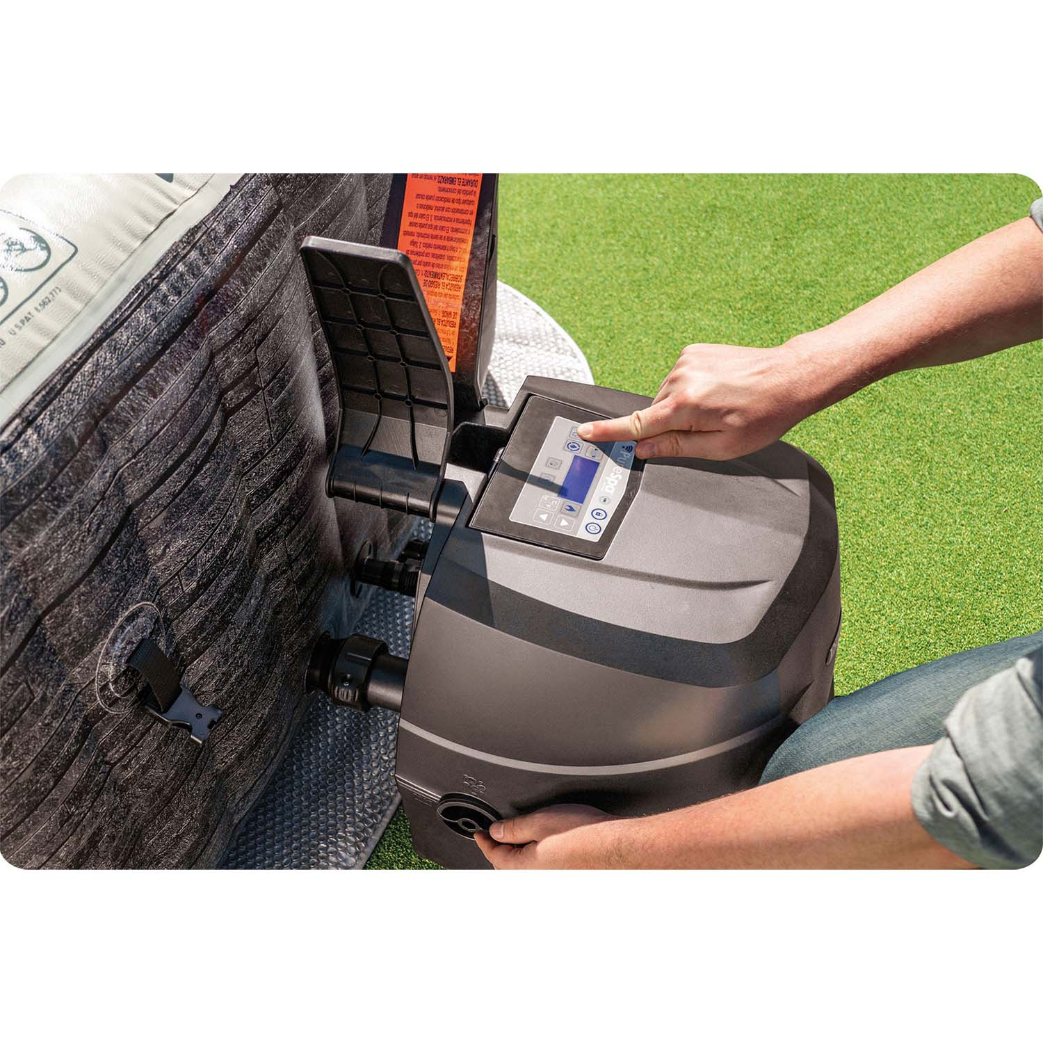 Ręka osoby naciska przycisk na panelu sterowania wanny z hydromasażem. Wanna jest czarna, a tło to zielona trawa.