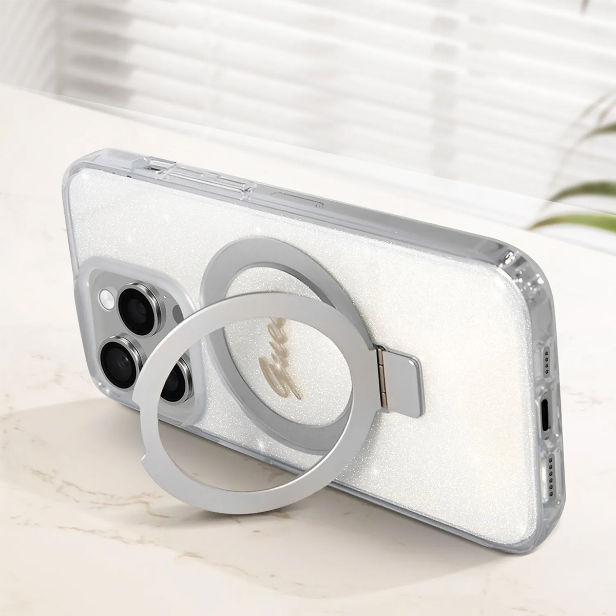 Un telefono in una custodia bianca scintillante con un supporto ad anello argentato. Il supporto è aperto, appoggiando il telefono su una superficie di marmo.