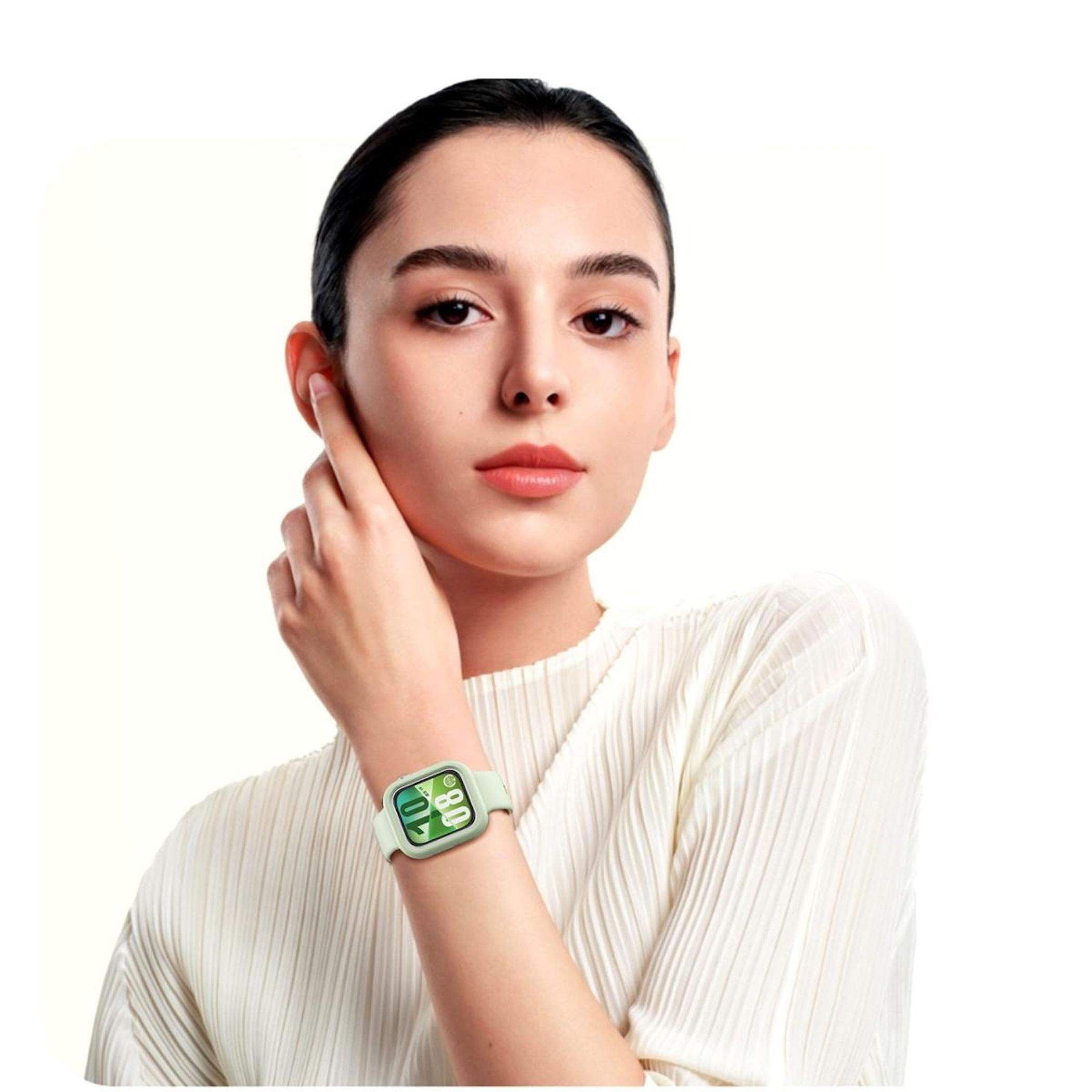 Una donna con smartwatch verde. Si tocca l'orecchio con una mano, guardando la fotocamera. Sfondo bianco.