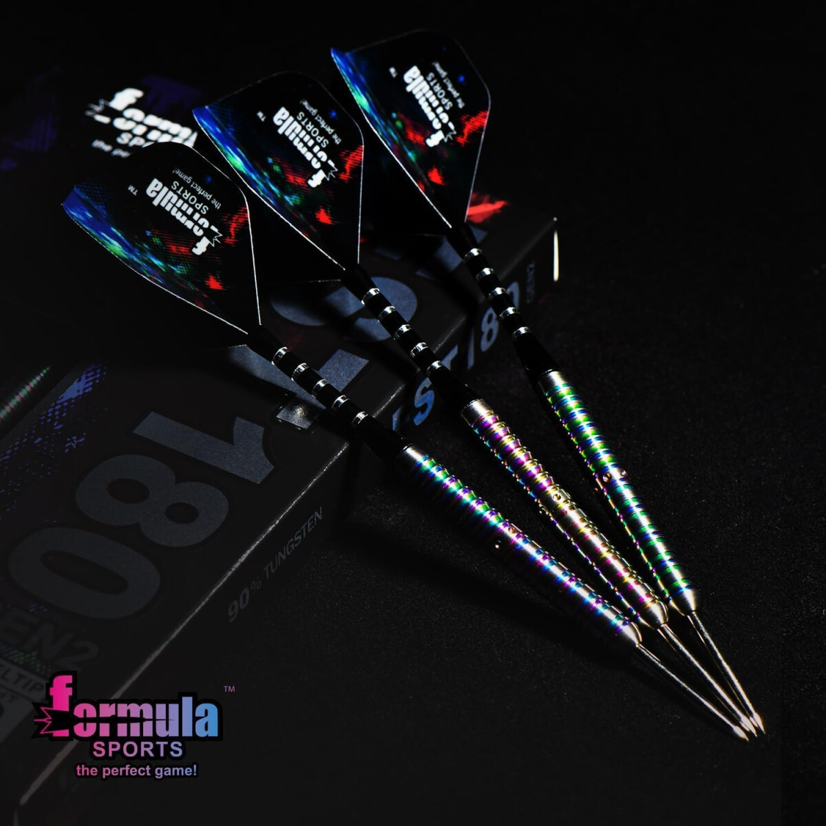 Four darts with colorful shafts and black flights are on a black surface next to a box with the text '180' and 'Formula Sports'.