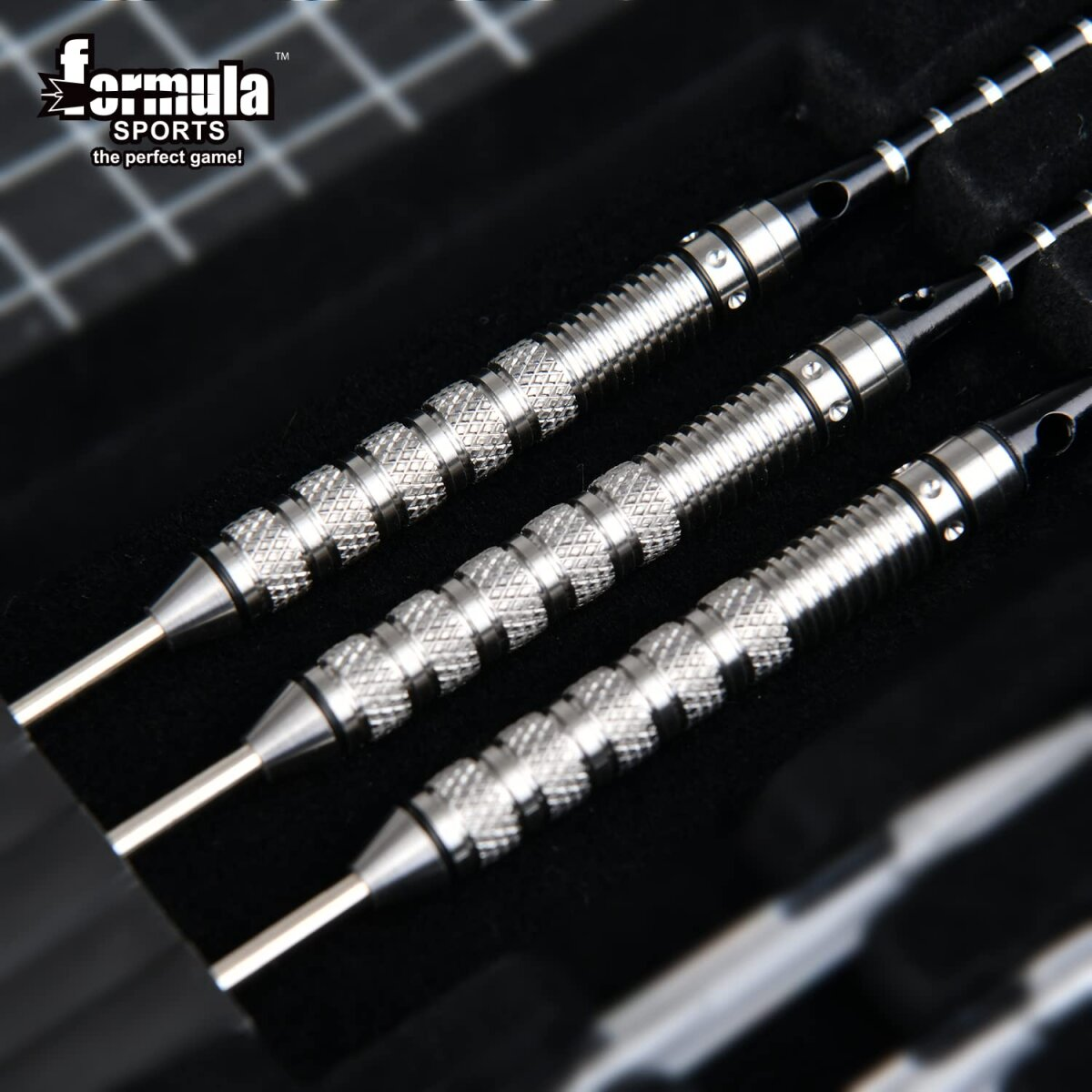 Close-up shot of three silver darts in a black case. 'Formula Sports' logo in the upper left corner.